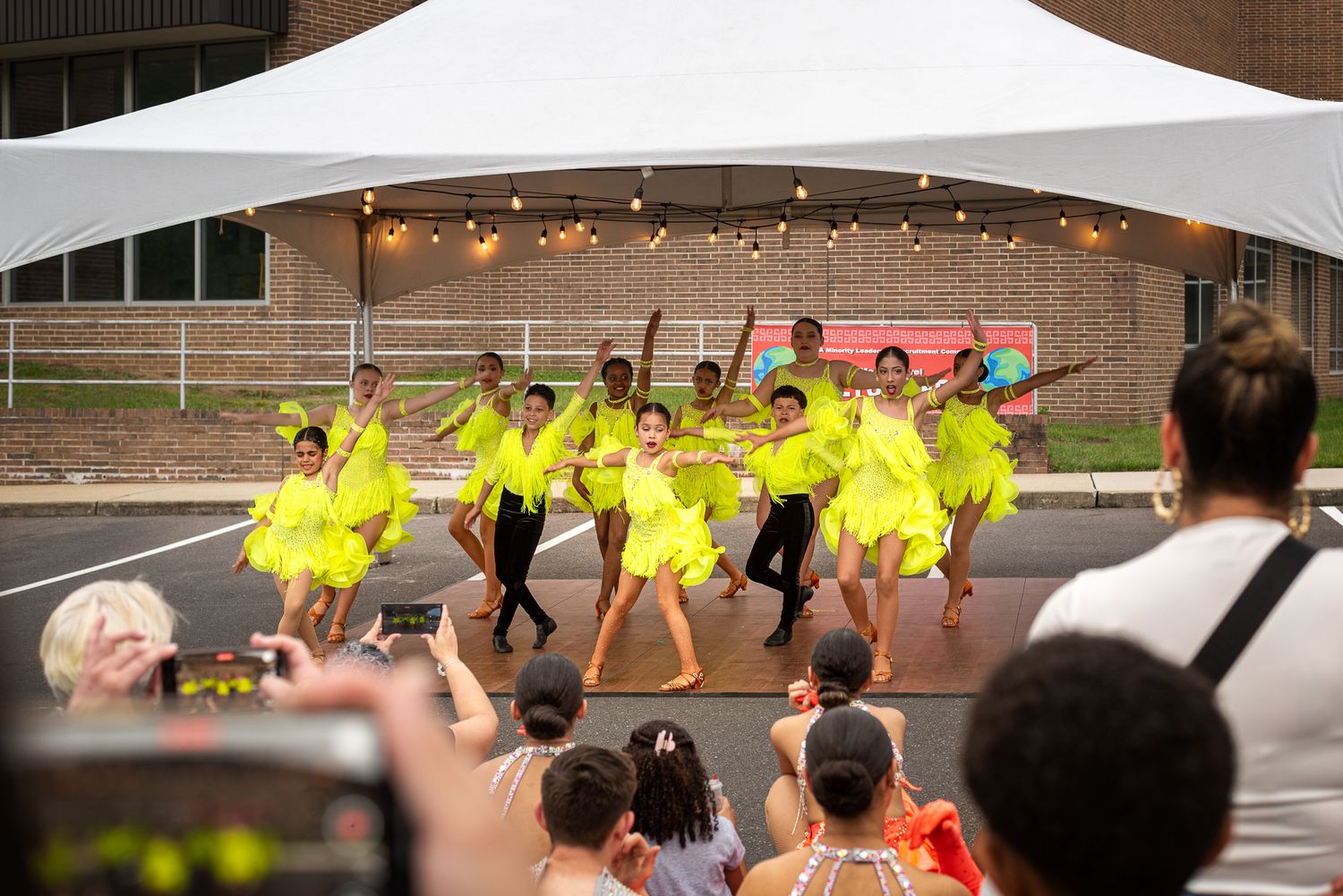 Group of dancers in yellow costumes performing outdoors at a community event.