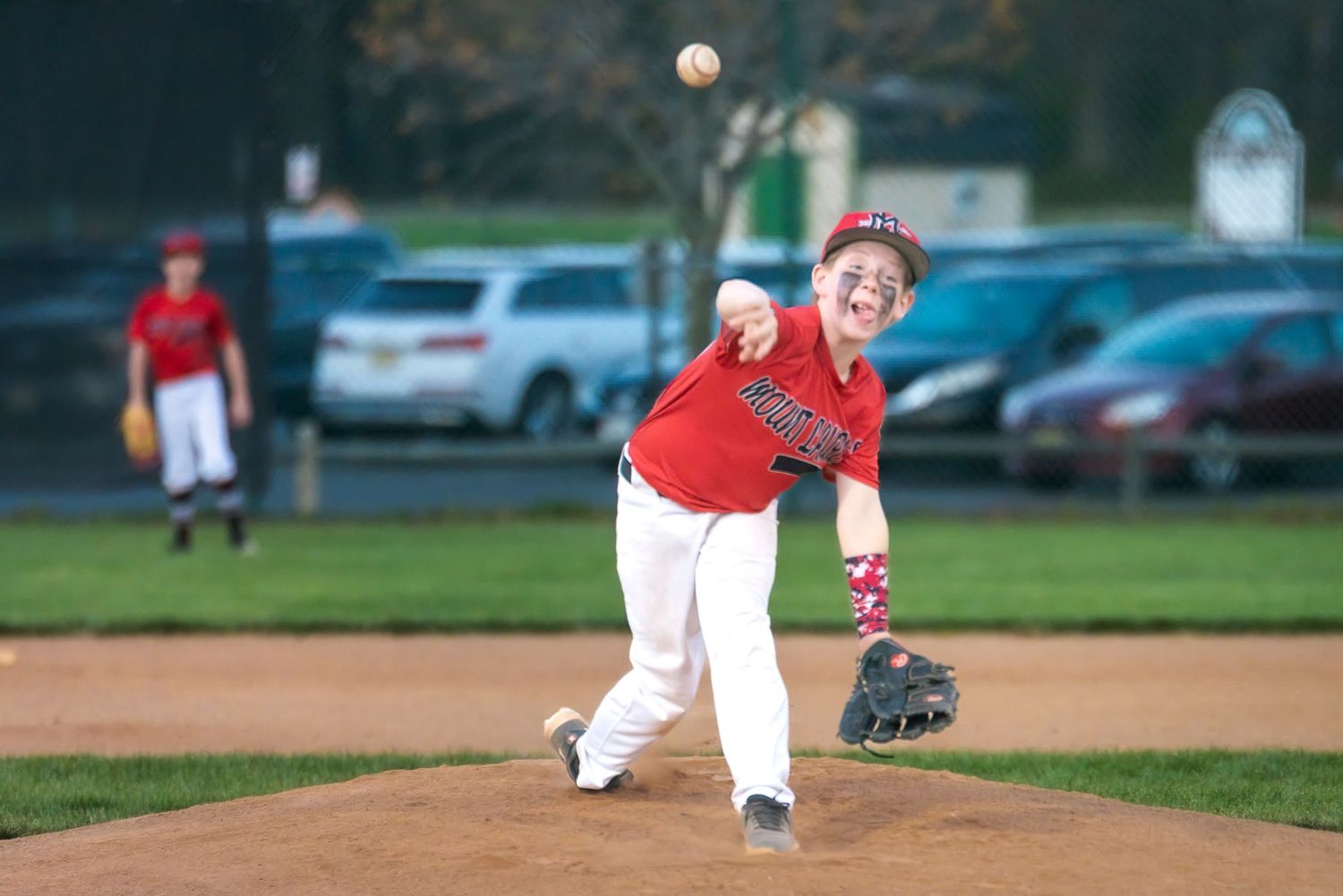 Young pitcher in red uniform delivers pitch during little league baseball game.