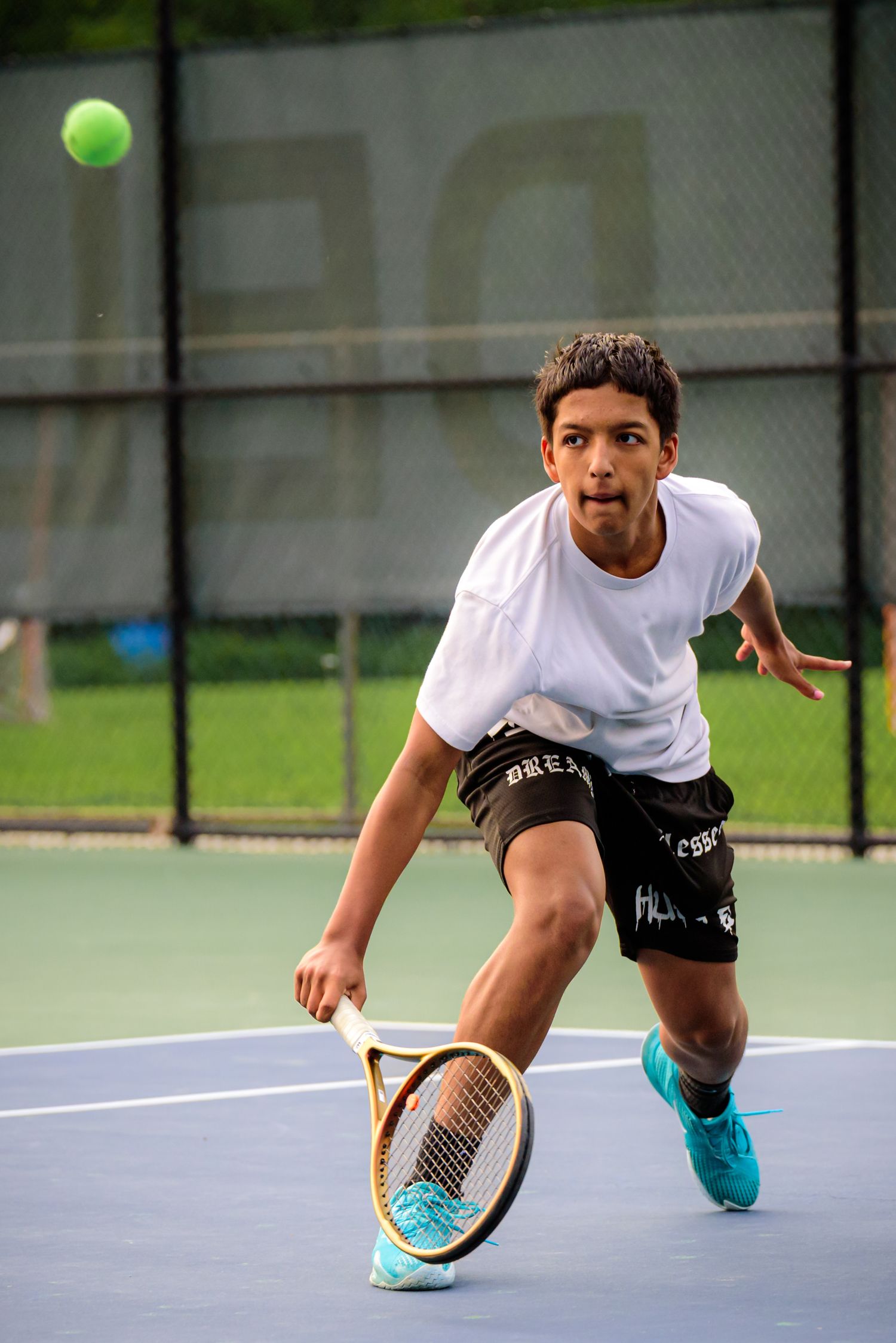 Tennis player in white shirt and black shorts stretches low to return a shot on blue court.