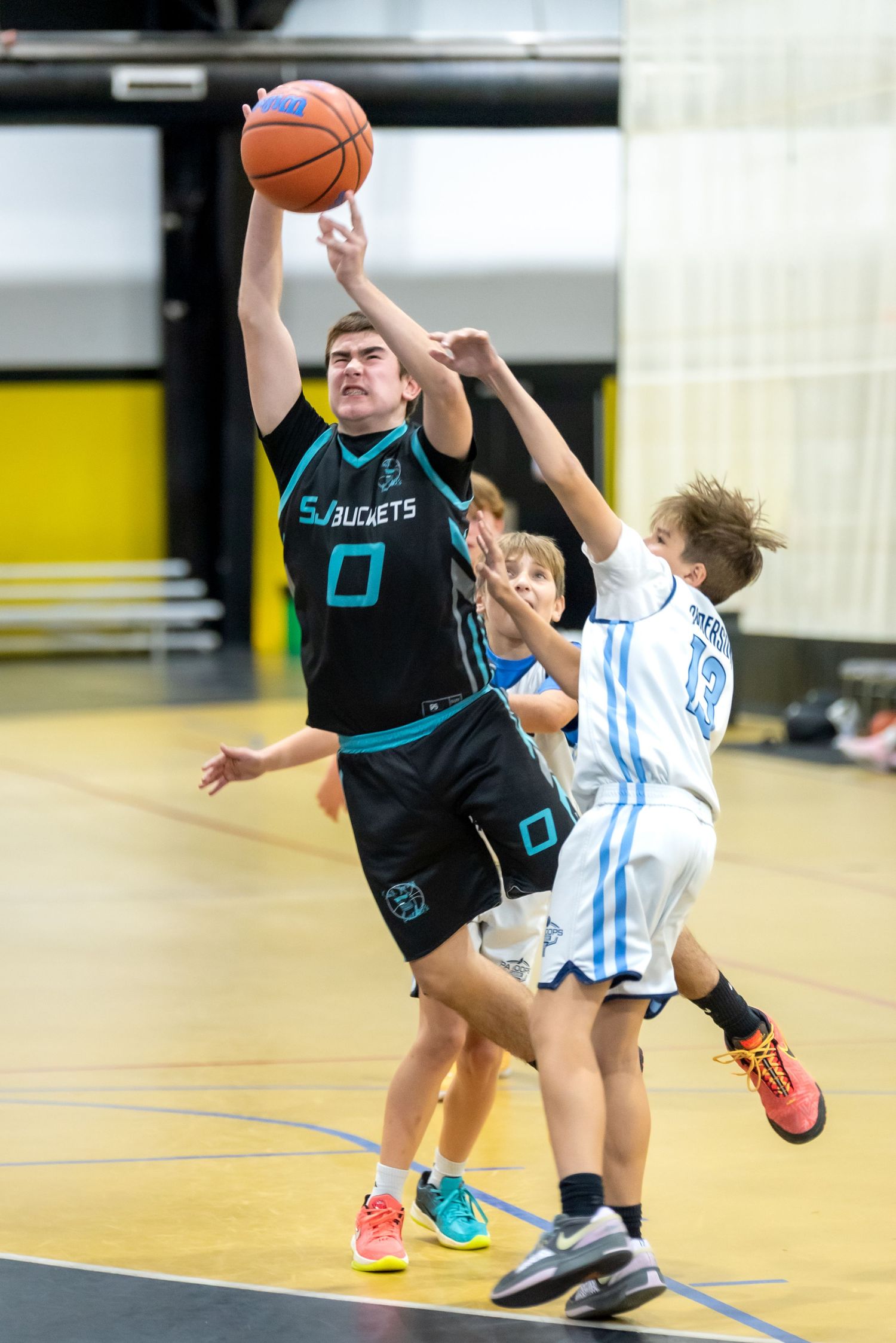 Youth basketball player in black Buckets jersey #0 leaps for a layup during an indoor game.