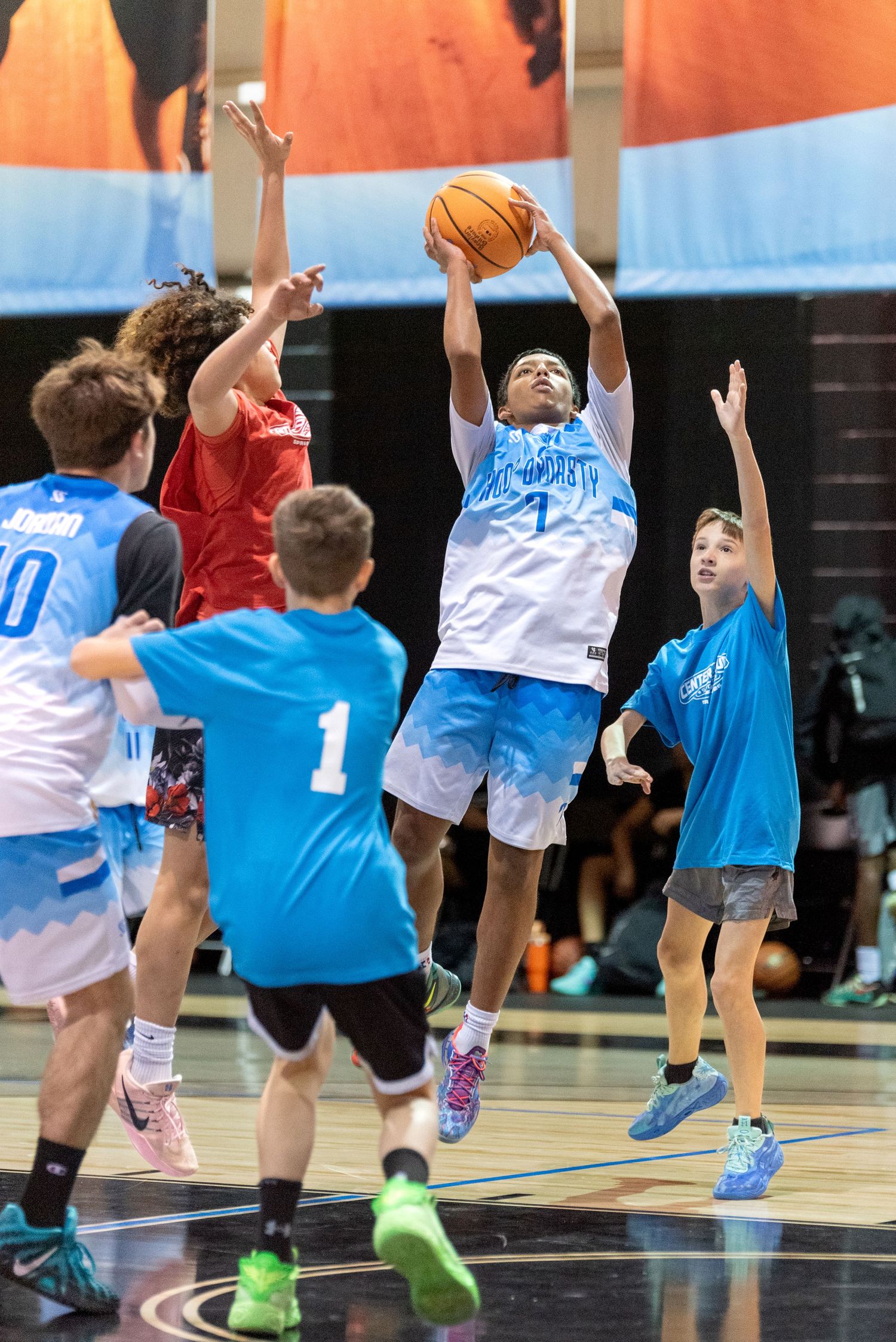 Young basketball players compete in an indoor game, with one player jumping to shoot the ball during a youth tournament.