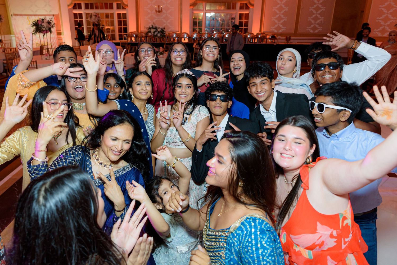 Crowded dance floor with guests celebrating at a festive party with colorful lighting.