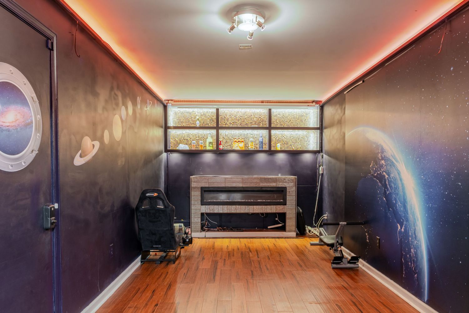 Space-themed game room with galaxy murals, electric fireplace, LED lighting, and hardwood floors.