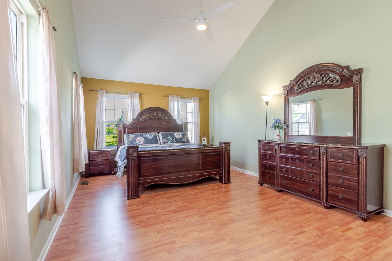 Spacious bedroom with vaulted ceiling, hardwood floors, and dark cherry wood furniture set including dresser with mirror.