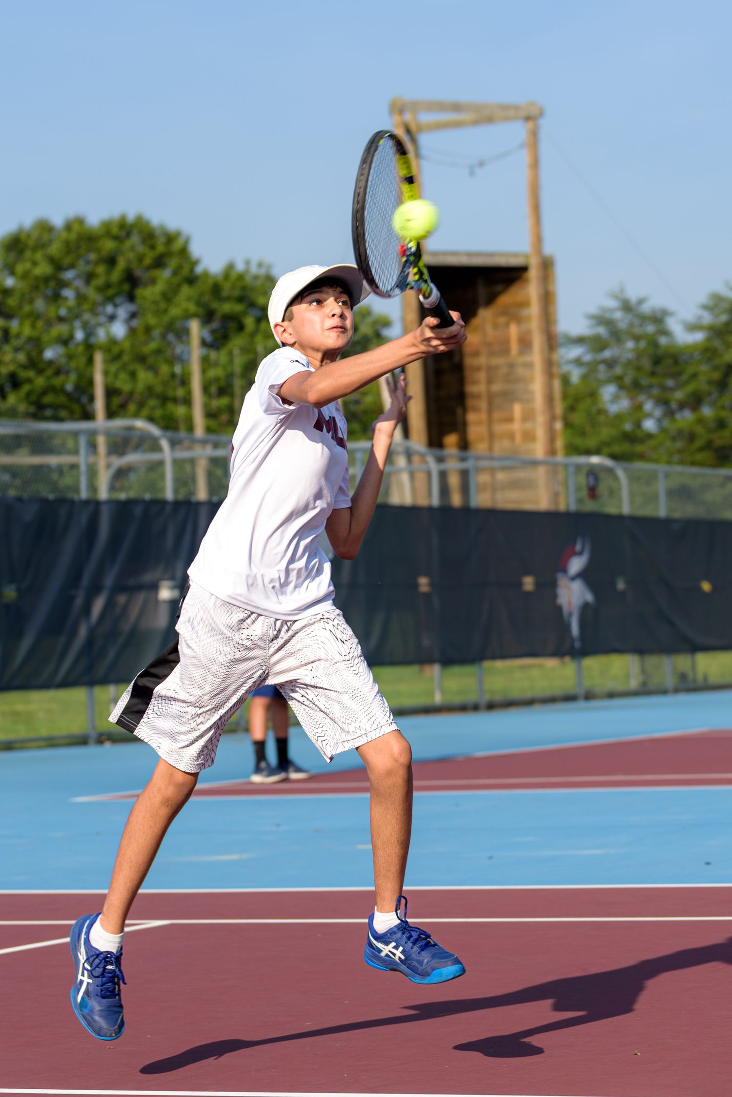 Tennis player in white uniform serves ball on blue outdoor court in sequence of action shots.