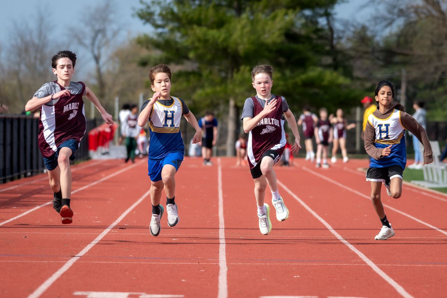 Young athletes compete in a sprint race on a red track during an outdoor middle school track and field meet.