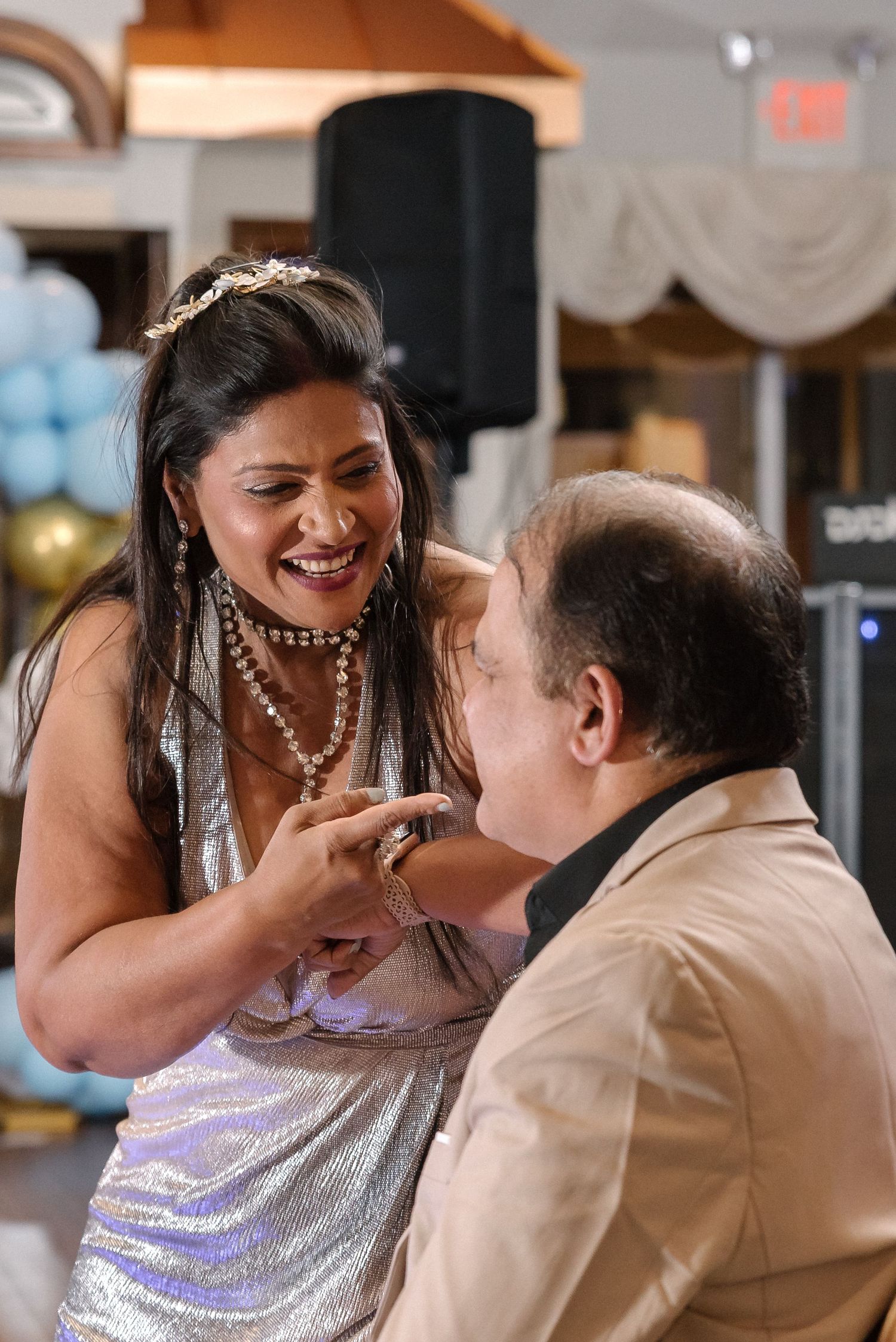 Couple sharing playful dance moves in sparkly formal attire at an indoor celebration.