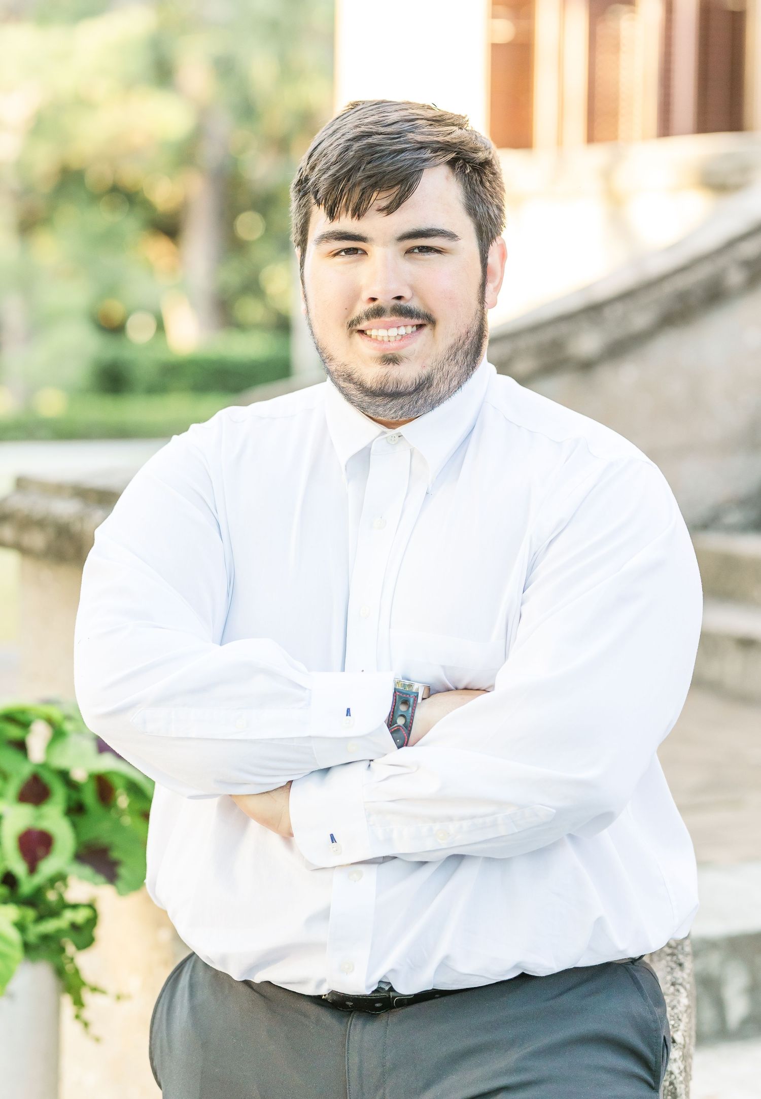 Portrait of someone in a crisp white dress shirt standing outdoors with crossed arms.