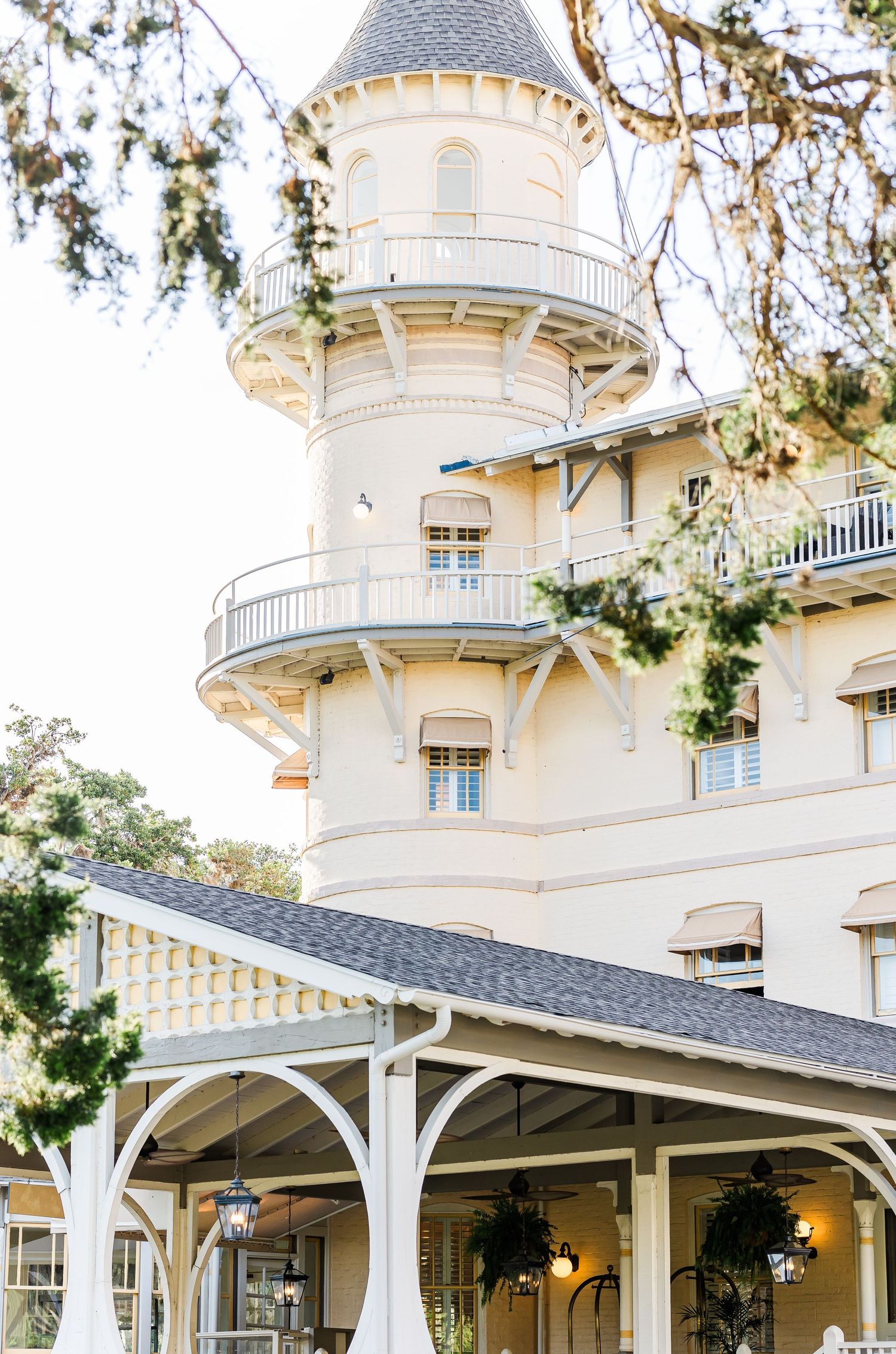 Elegant white Victorian-style mansion with wraparound porch and ornate architectural details against a tree-lined backdrop.