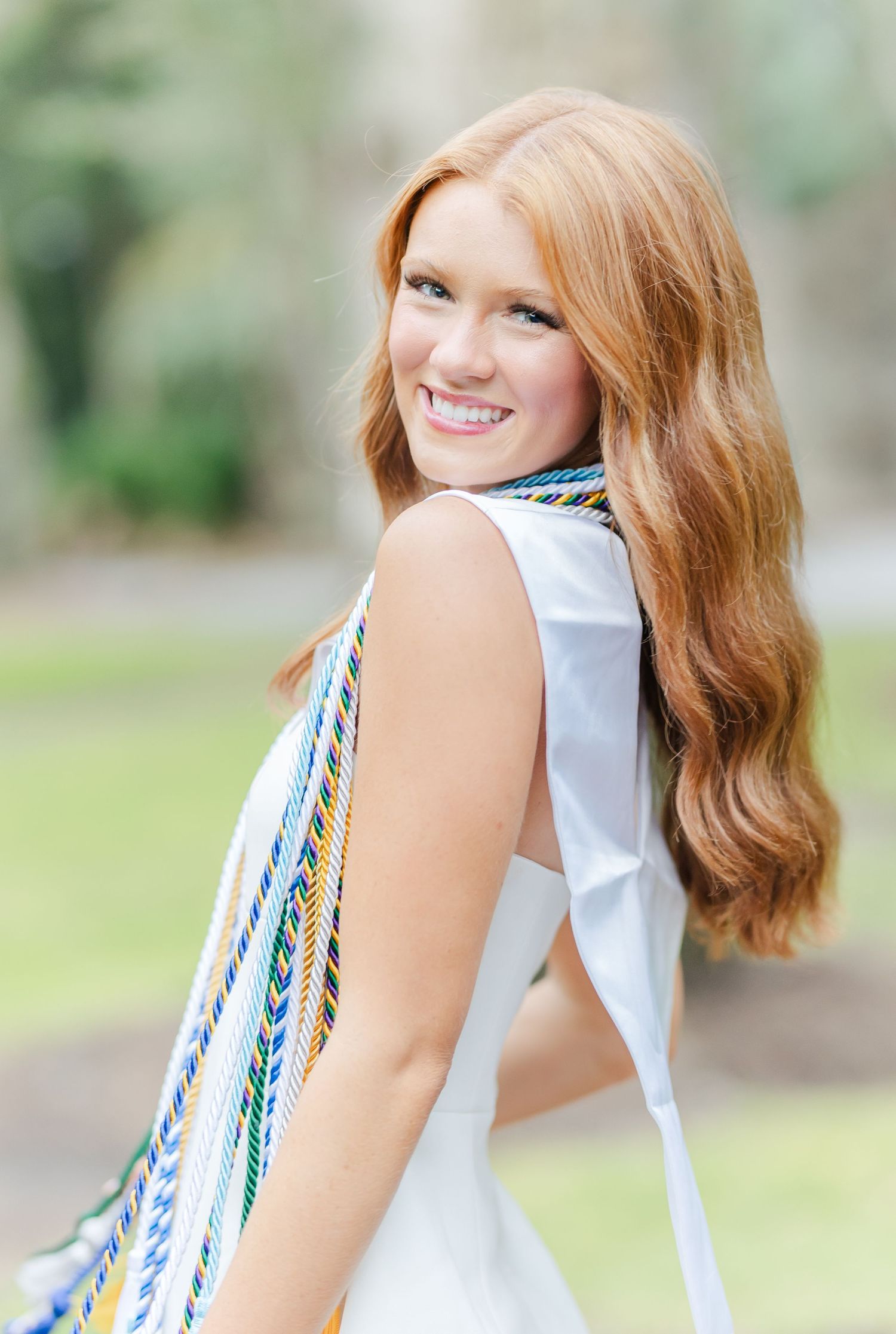 Woman in sleeveless white dress with blue trim poses playfully against outdoor garden background.