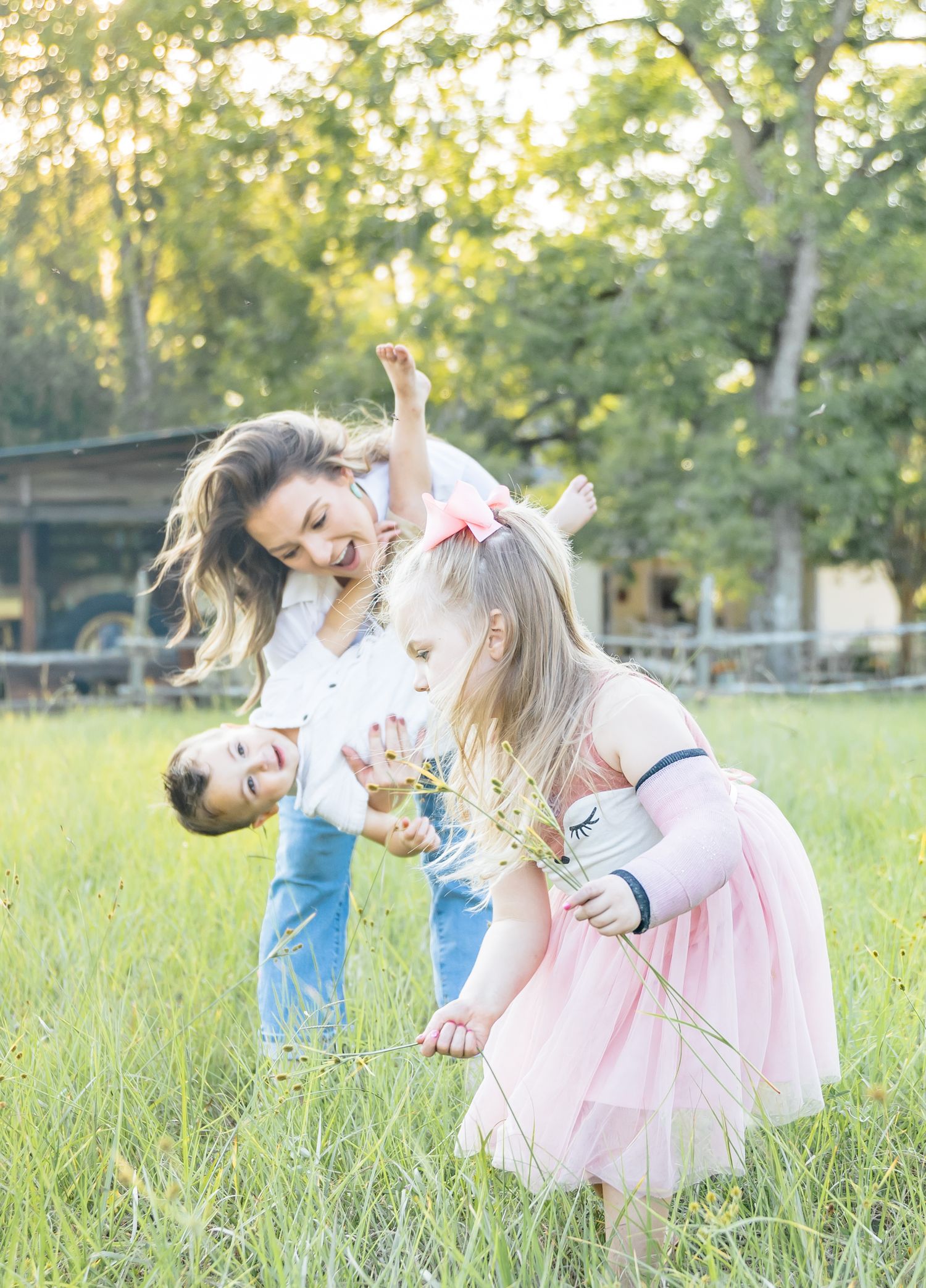 People in coordinating blue and pink outfits embrace lovingly in a sunlit grassy field during golden hour.