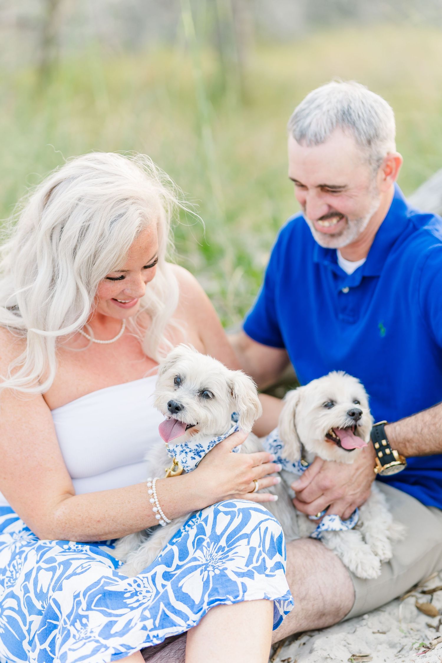 A couple in coordinating blue and white outfits shares tender moments with their small white dog outdoors.