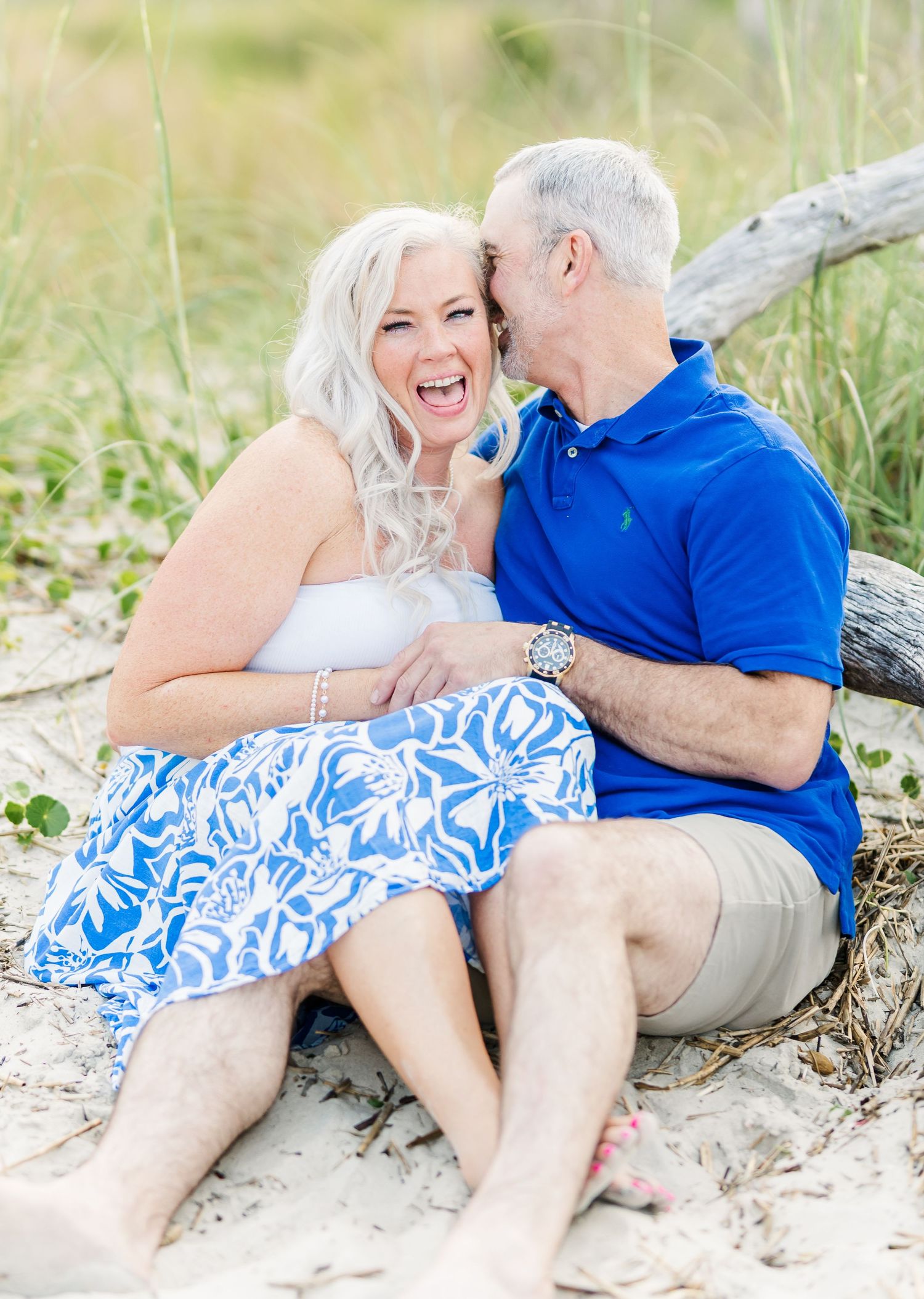 Playful couple relaxes on beach sand wearing coordinated blue and white summer outfits.