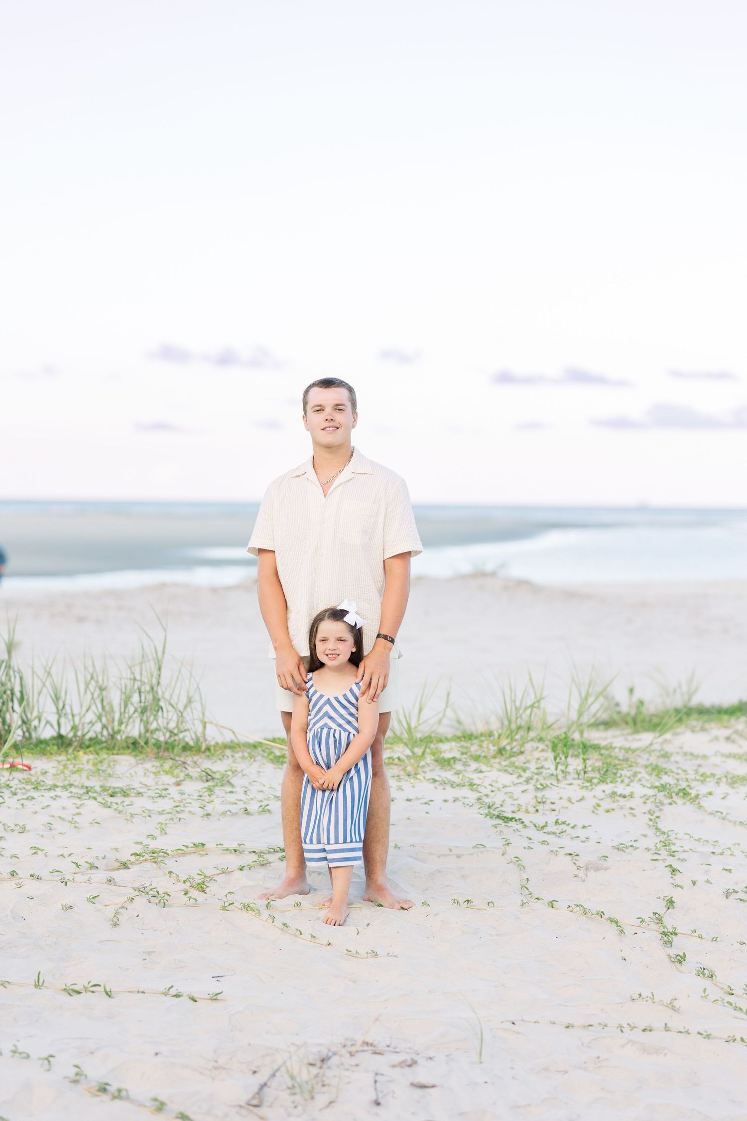 Family enjoying a summer day together on a sandy beach in casual white outfits.