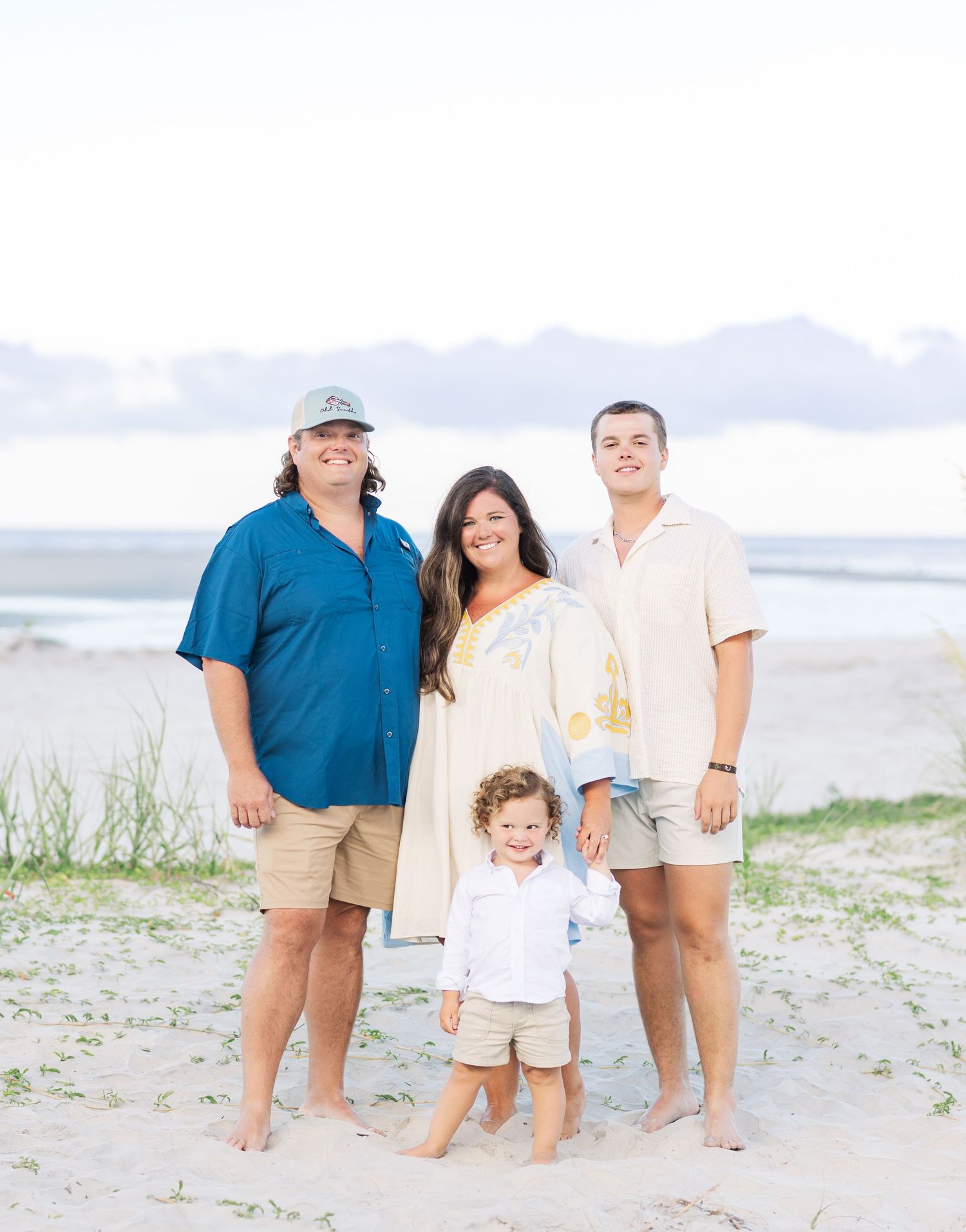A family of four poses together on a sandy beach wearing coordinated beach attire.