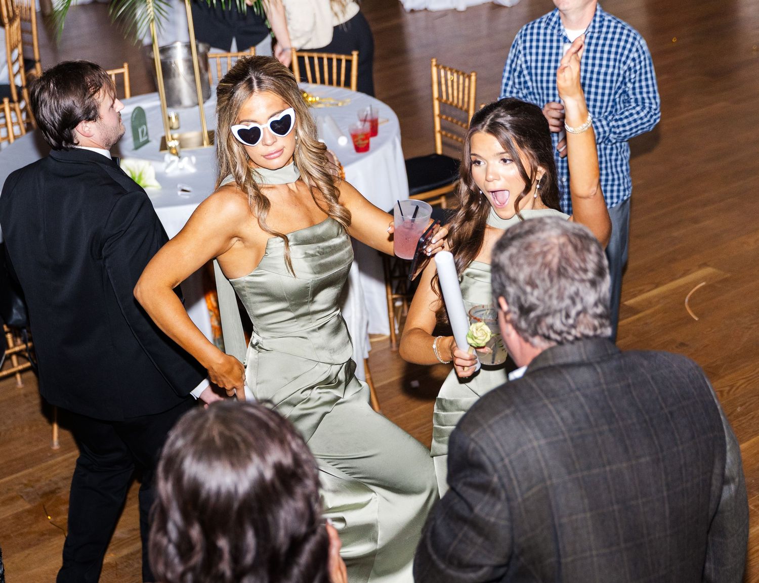 Two bridesmaids in sage green dresses dance and socialize with guests at elegant wedding reception.