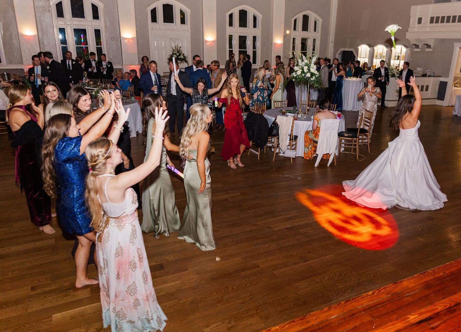 Bride tosses bouquet to eager wedding guests on a dance floor during reception celebration.