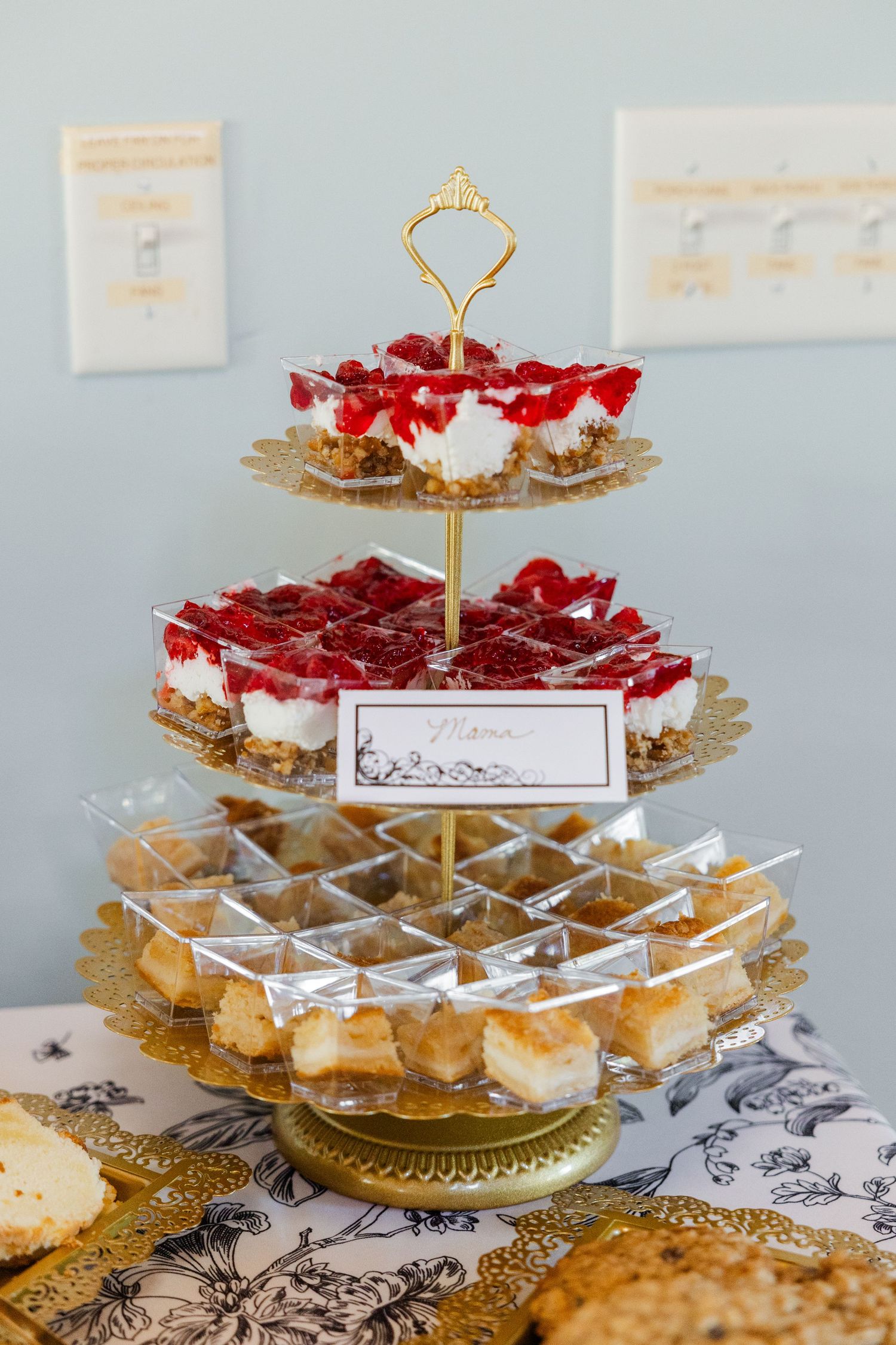 Three-tiered gold stand showcases strawberry cheesecake cups and mini pastries at an elegant dessert table.