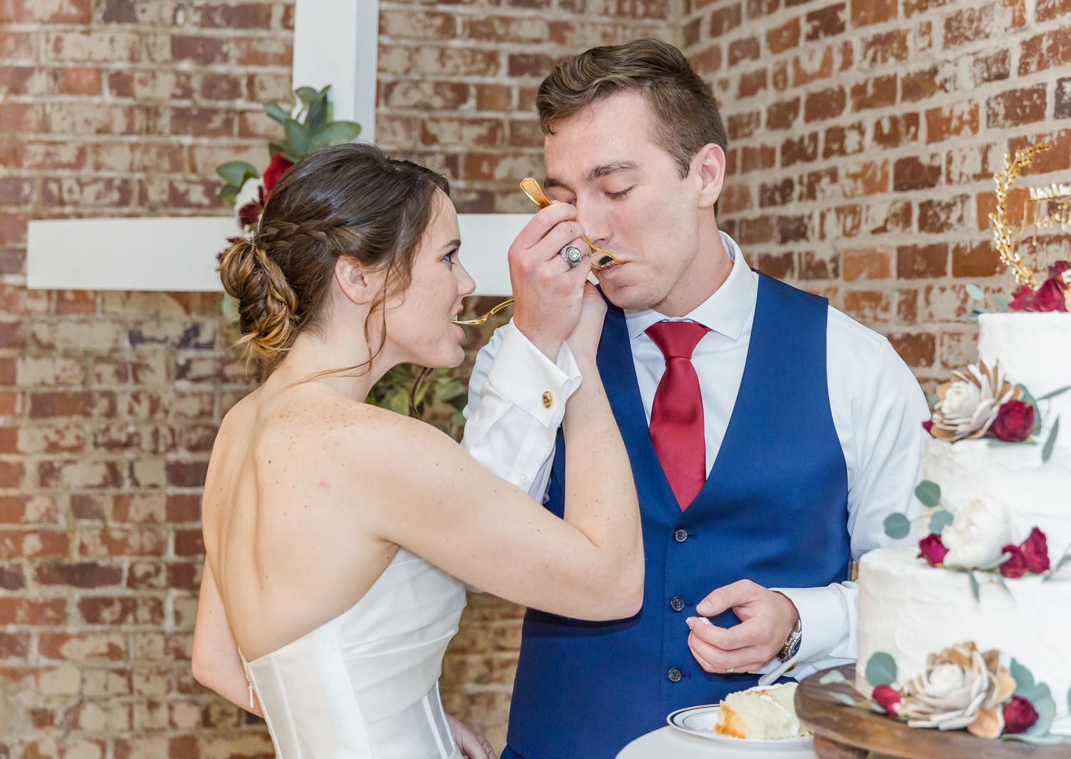 A couple shares tender moments while dining at their wedding reception in a rustic brick-walled venue.
