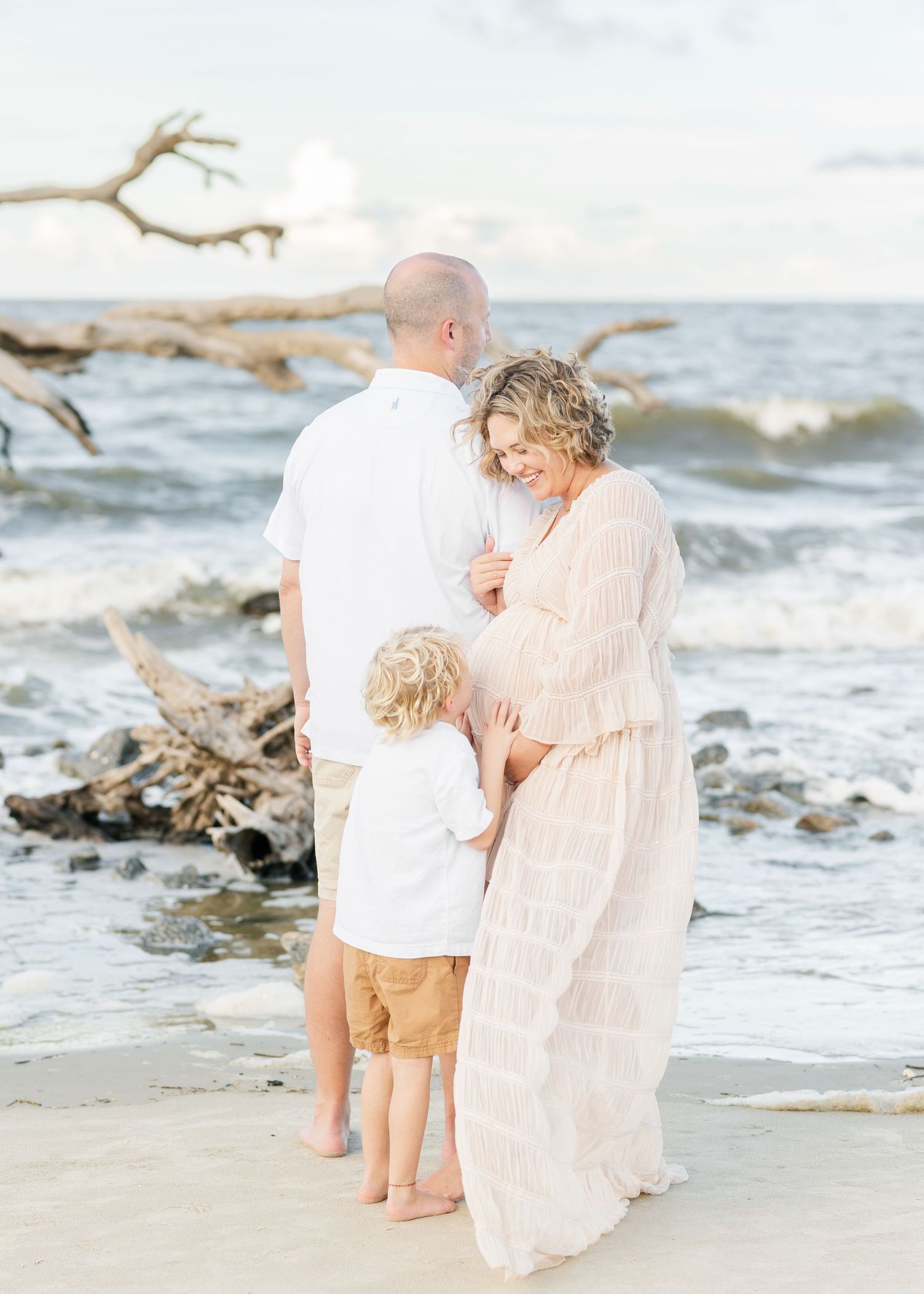 A beachside maternity session with a couple walking along the shoreline at sunset.
