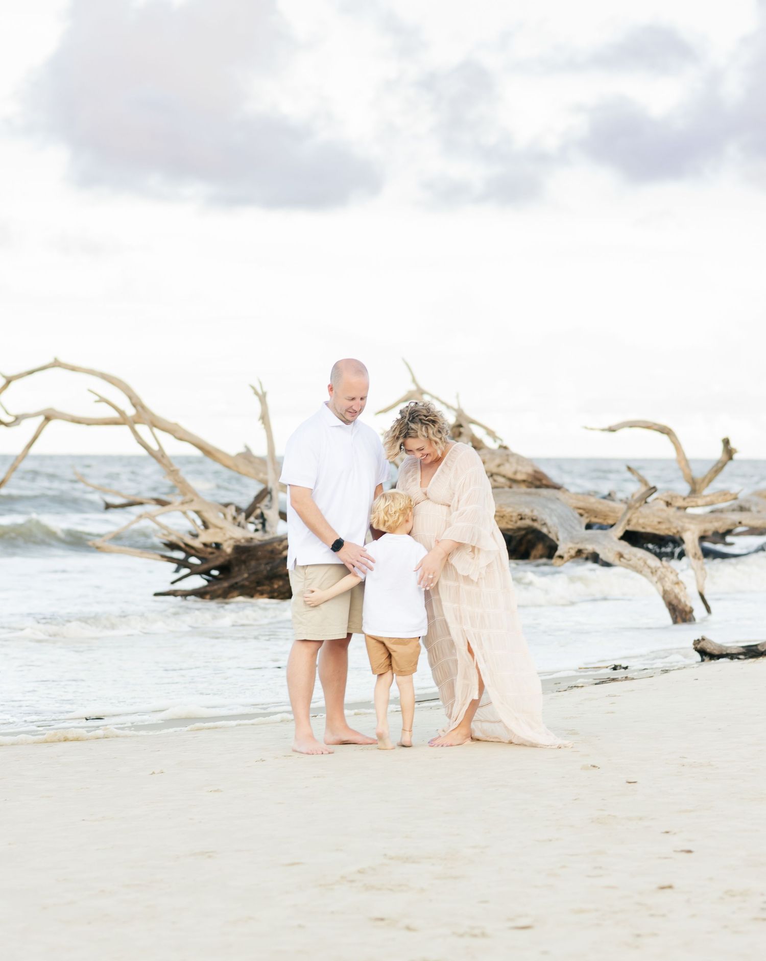 Family standing together on a beach with driftwood in soft, dreamy lighting.