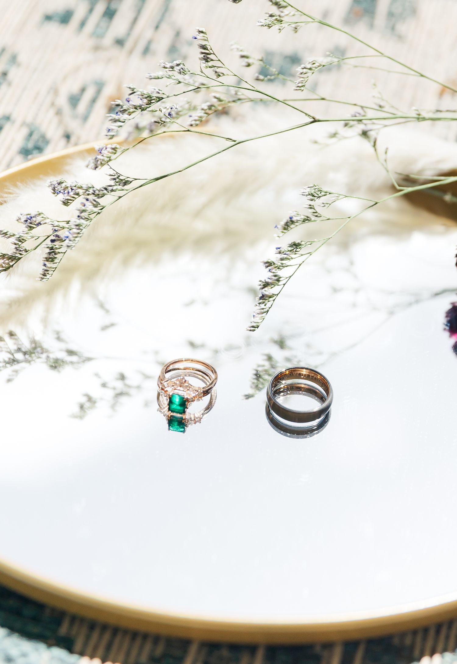 Wedding rings including an emerald stone ring displayed on white surface with soft baby's breath flowers.