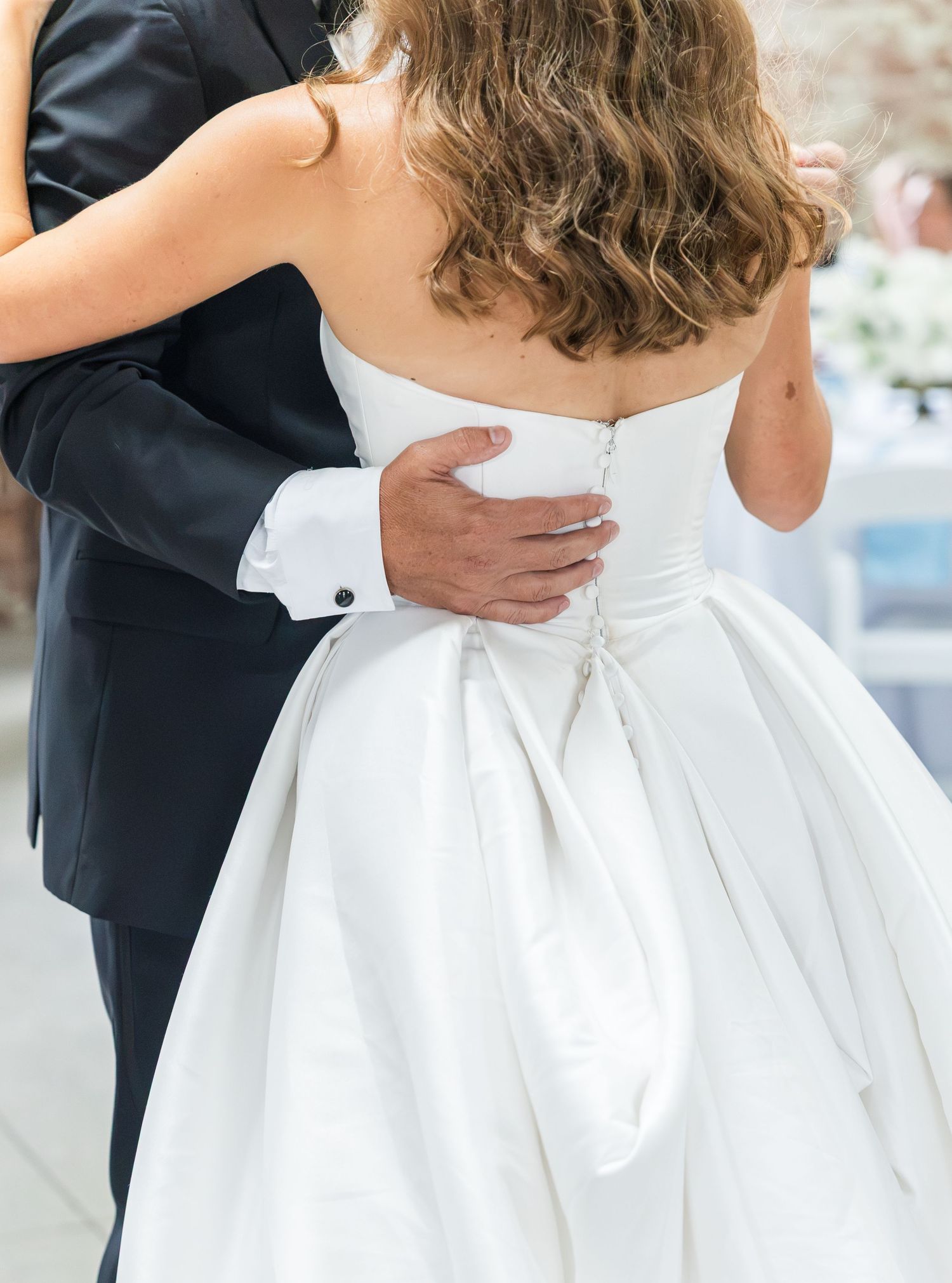Close-up of bride in strapless white ballgown dancing with groom in black tuxedo at reception.