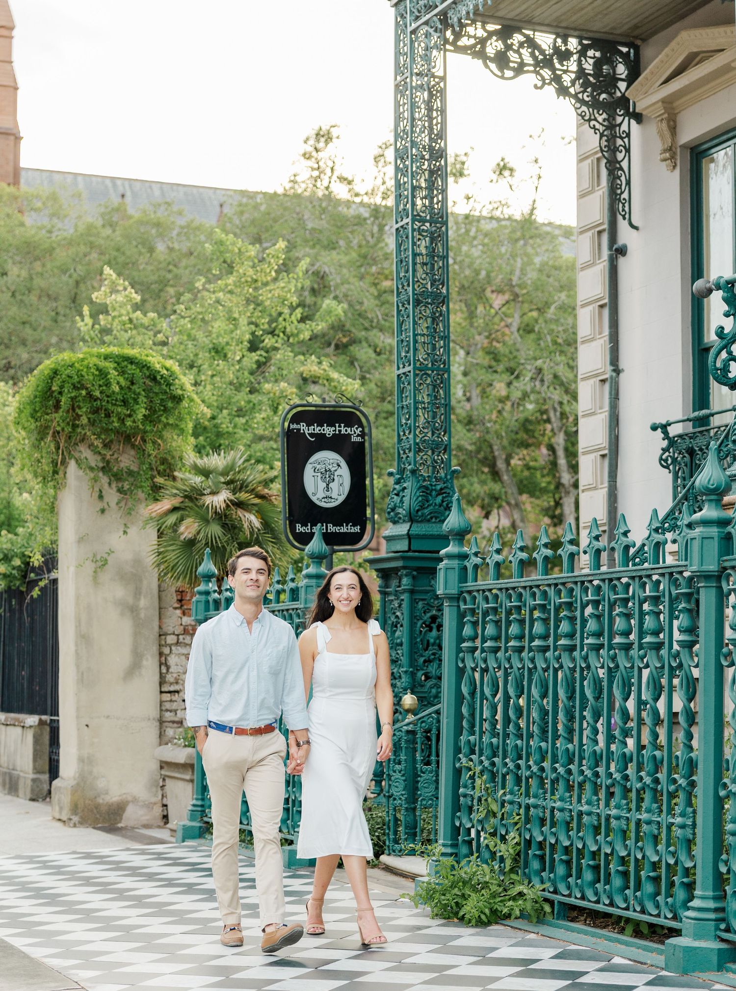 Couple walks together past ornate teal ironwork fence and B&B sign in historic Savannah, GA.