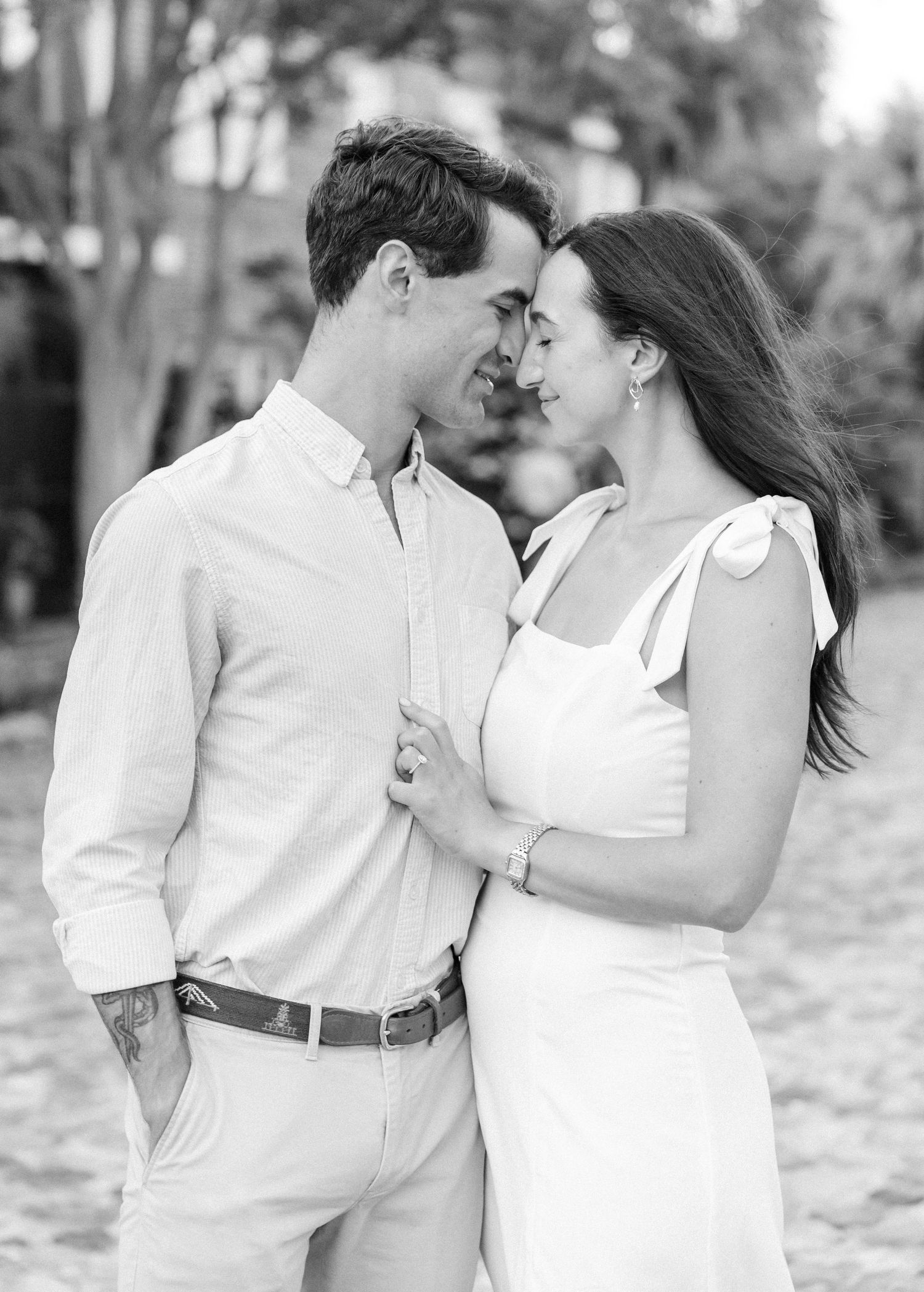 Black and white close-up of a couple gazing at each other tenderly, dressed in white outfits outdoors.