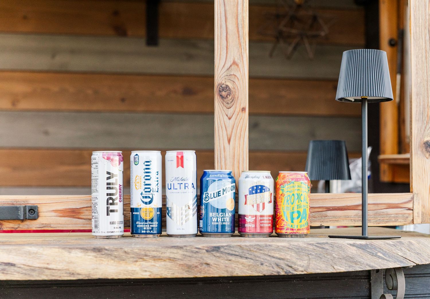 Assorted beer and seltzer cans including Truly, Corona, and Blue Moon displayed on a rustic wooden bar.