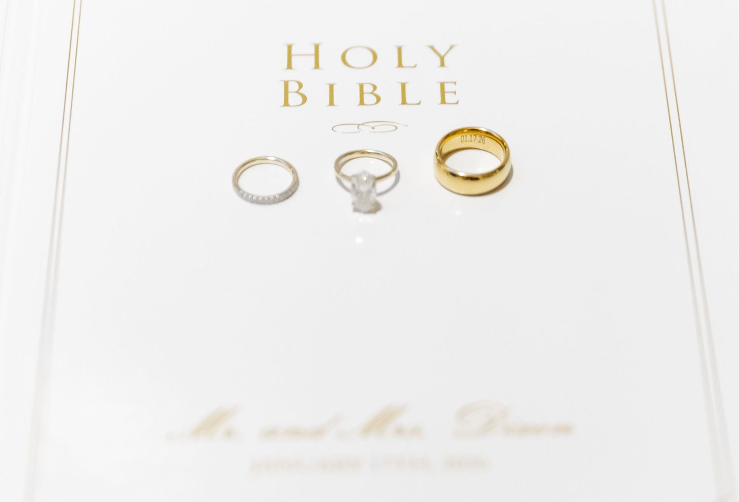 A Holy Bible lies open on a white surface with wedding rings placed above it.