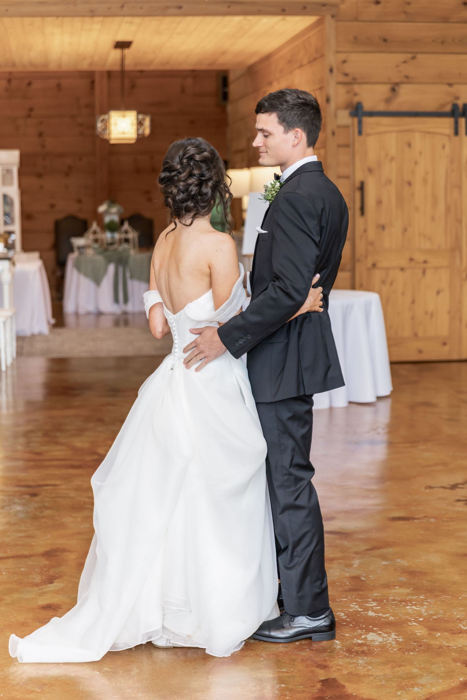 Wedding couple and attendants pose playfully on a polished wooden floor in a rustic barn venue.