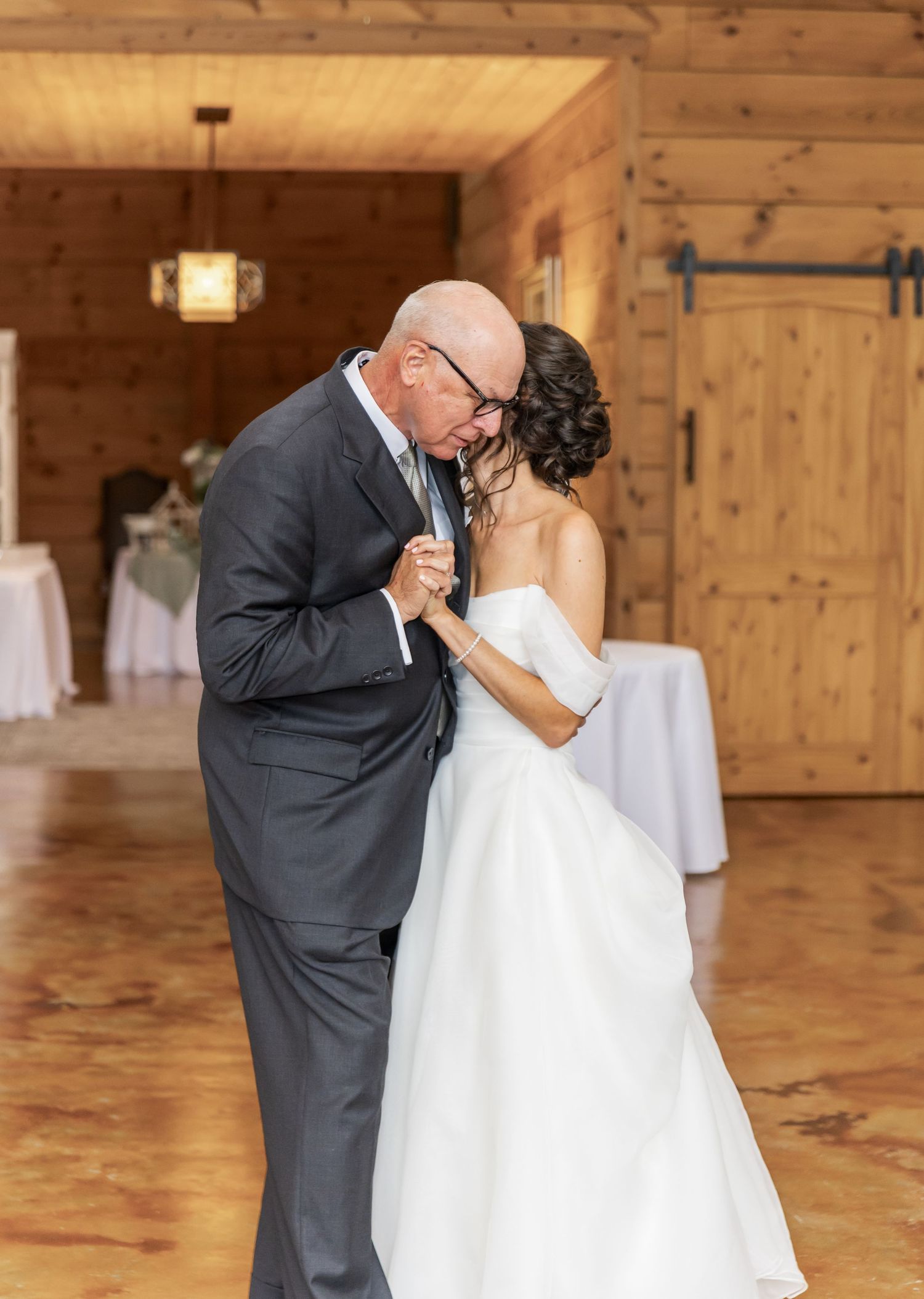 An emotional dance captured in a rustic wooden reception hall with elegant white decor.