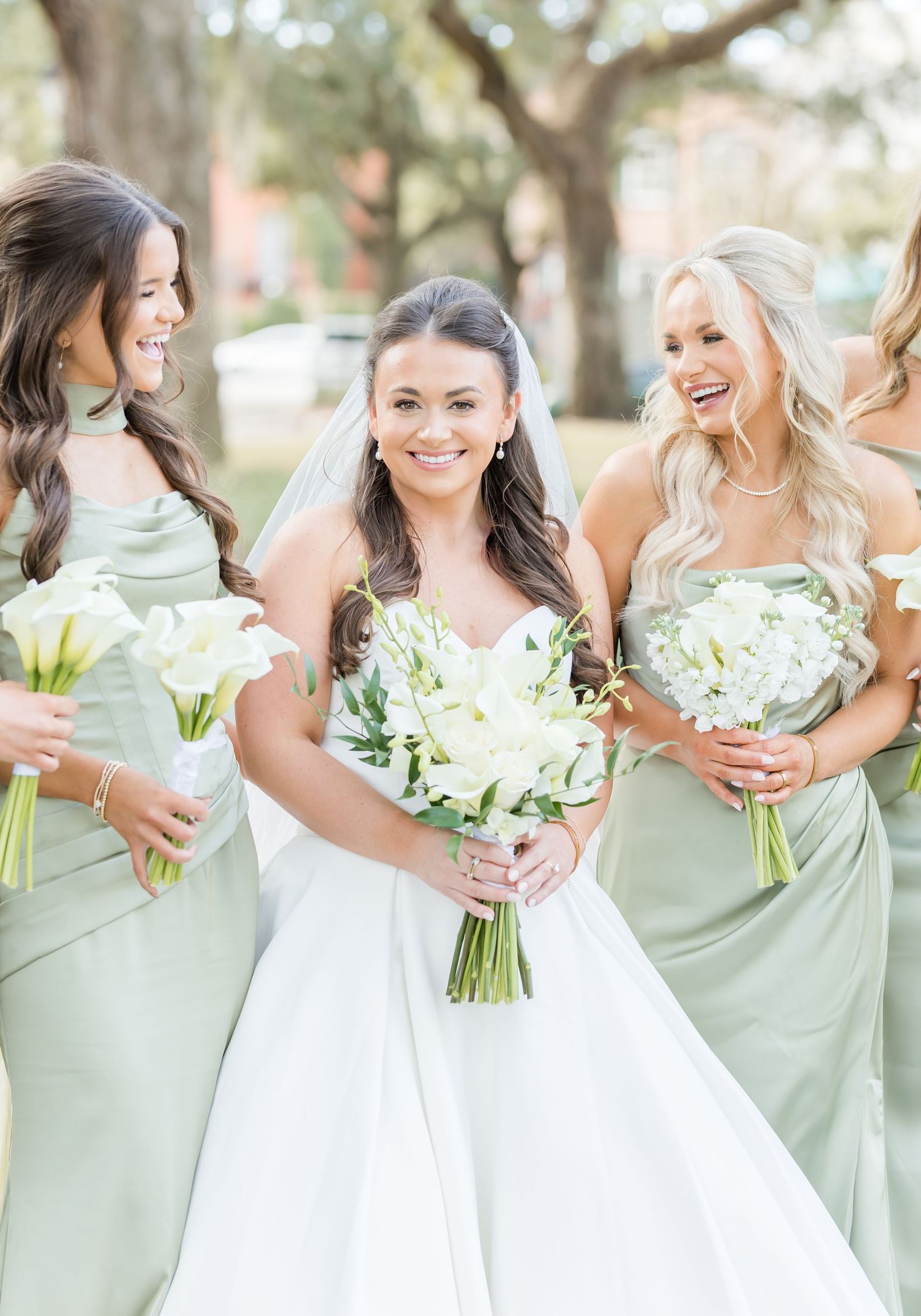 Joyful bridesmaids in mint green dresses laugh and pose with white floral bouquets outdoors.