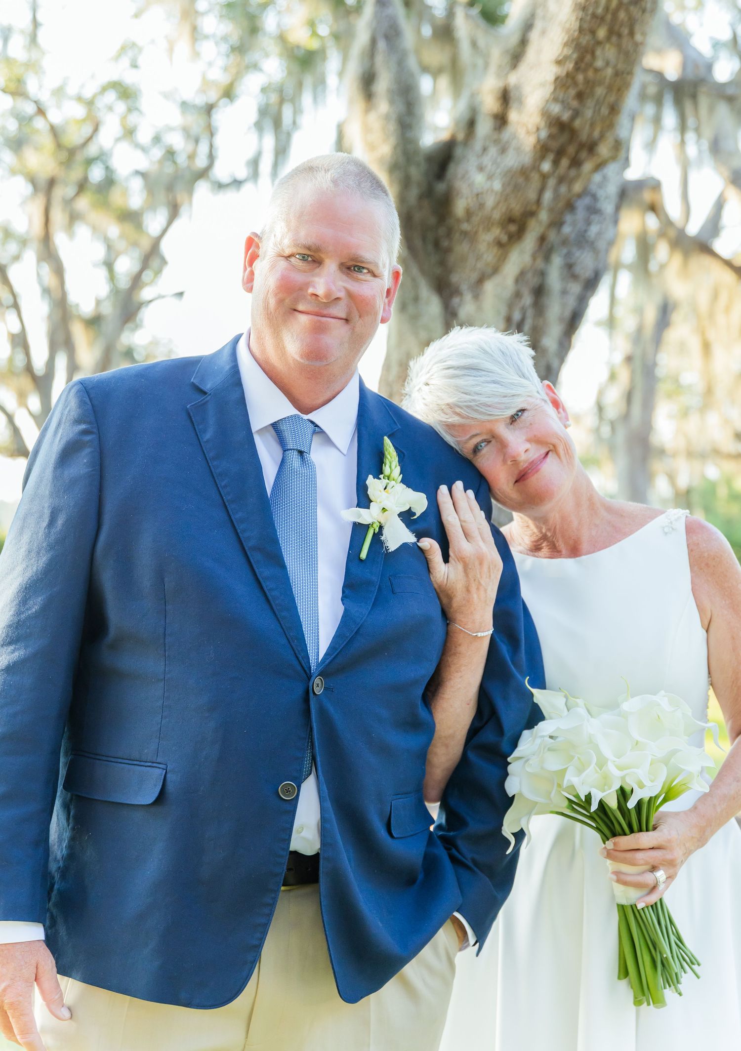 A happy couple shares joyful moments in their wedding attire against a backdrop of Spanish moss-draped trees.