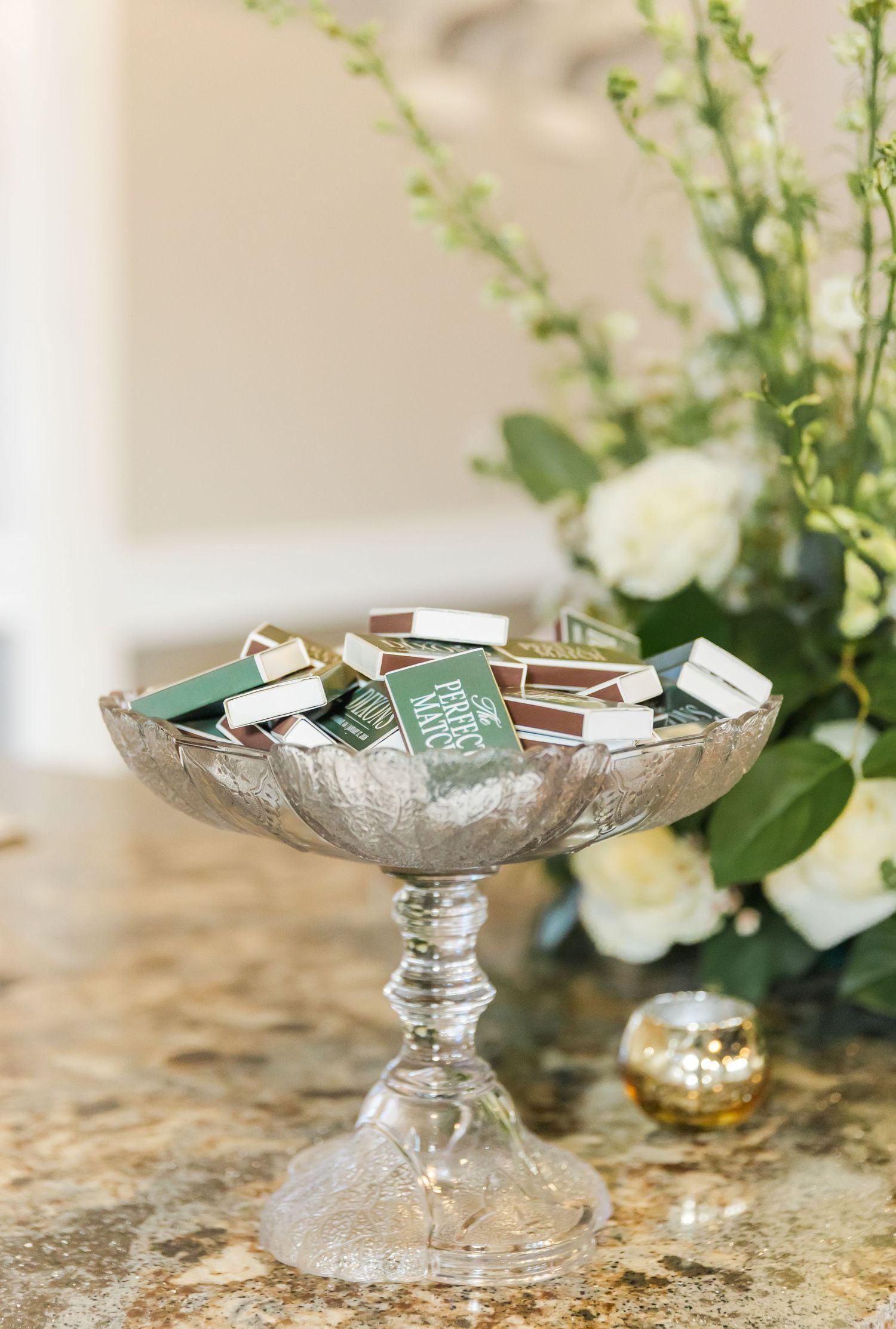 Crystal pedestal bowl filled with wedding favor cards on a marble surface.