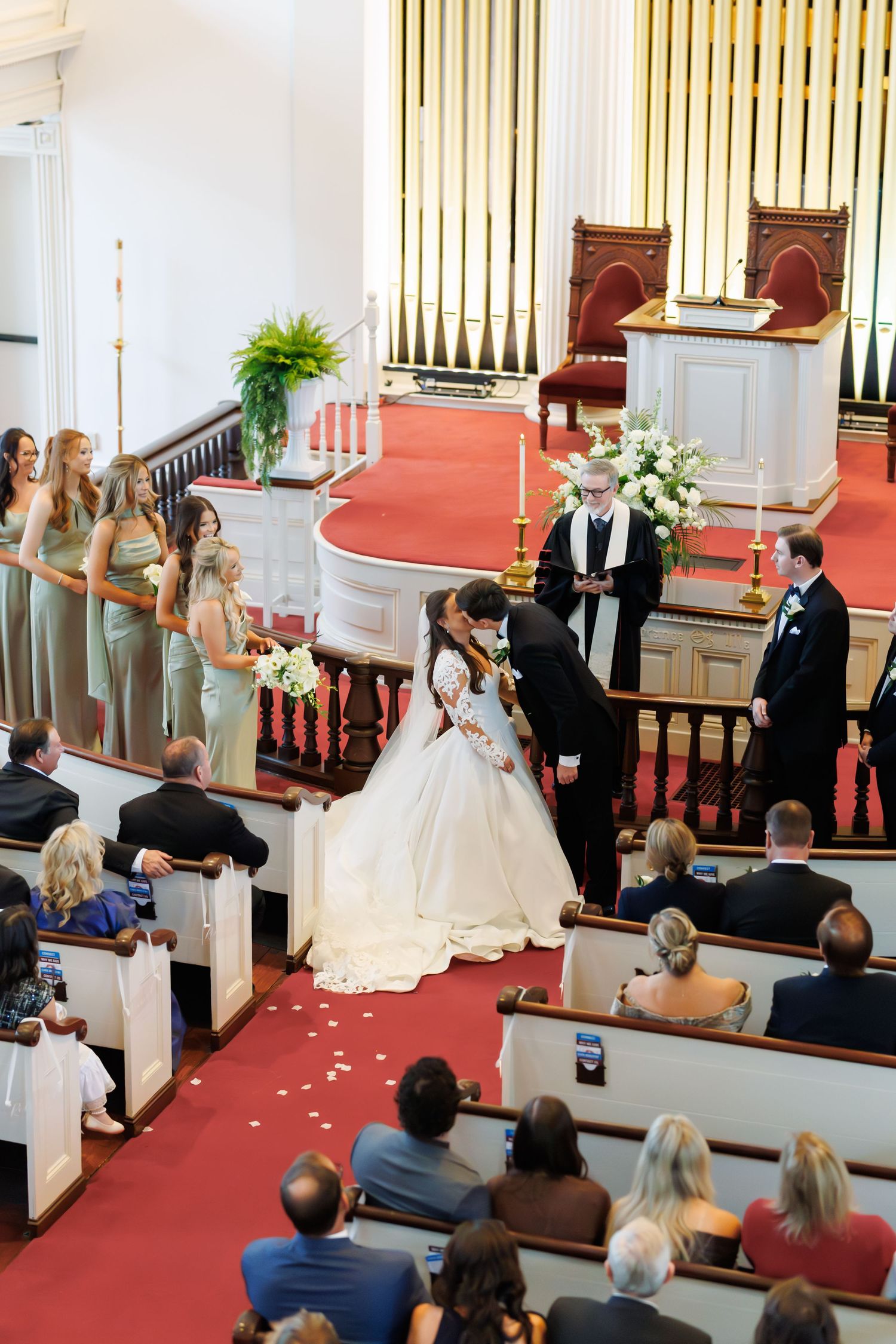 Wedding ceremony in a traditional church with red carpet aisle and white floral decorations.