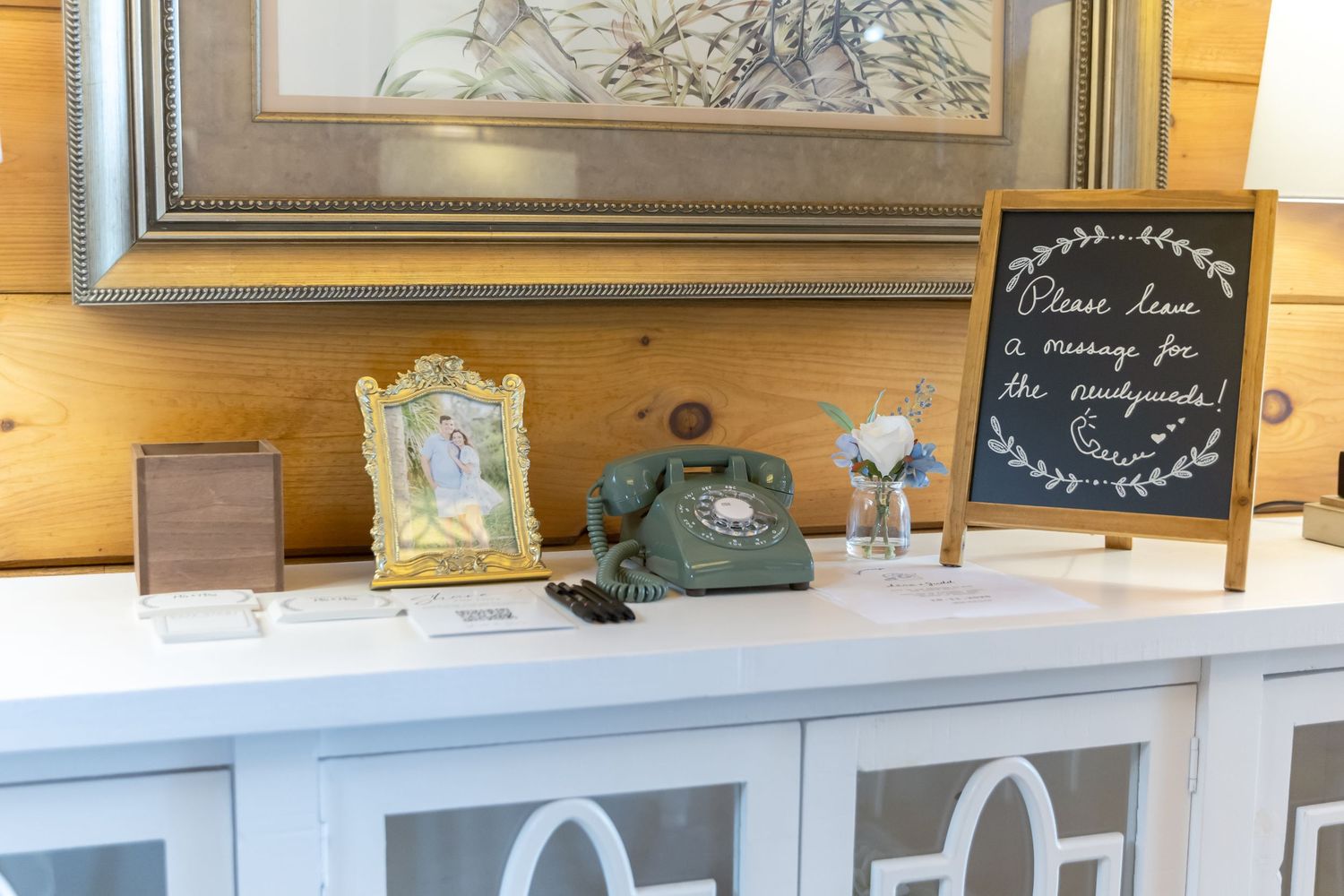 A rustic farmhouse style kitchen counter with white cabinets, wooden walls, and decorative items on display.