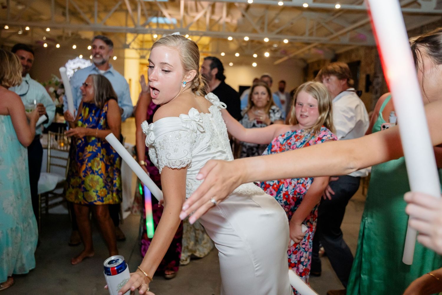 Wedding celebration with dancers holding glowing foam sticks under string lights.