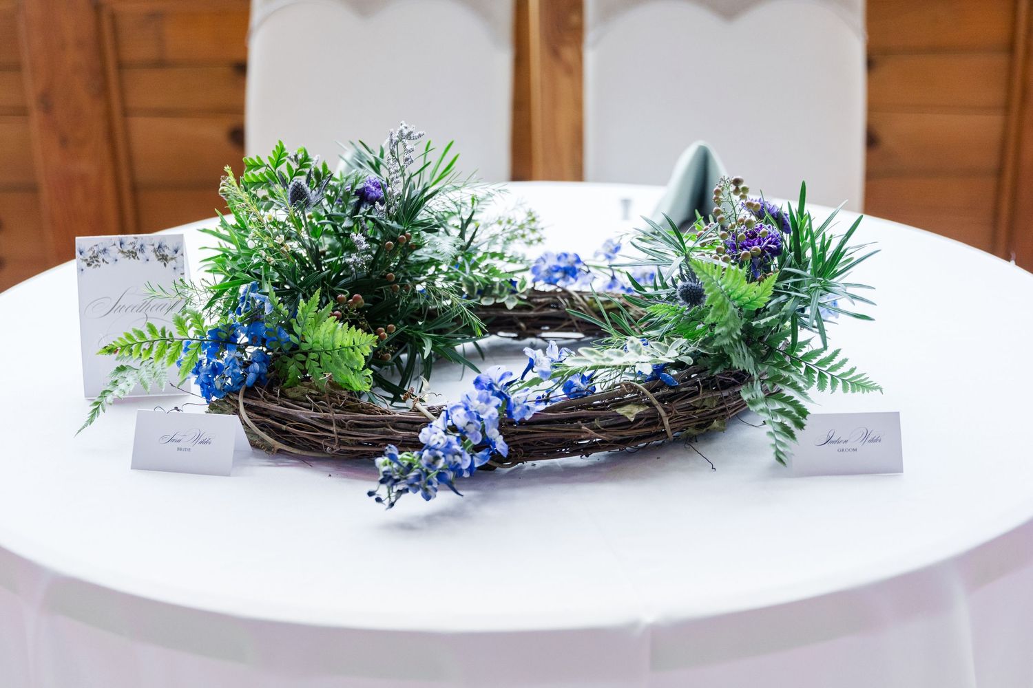 Small grapevine wreath decorated with blue and white flowers and greenery for spring home decor.