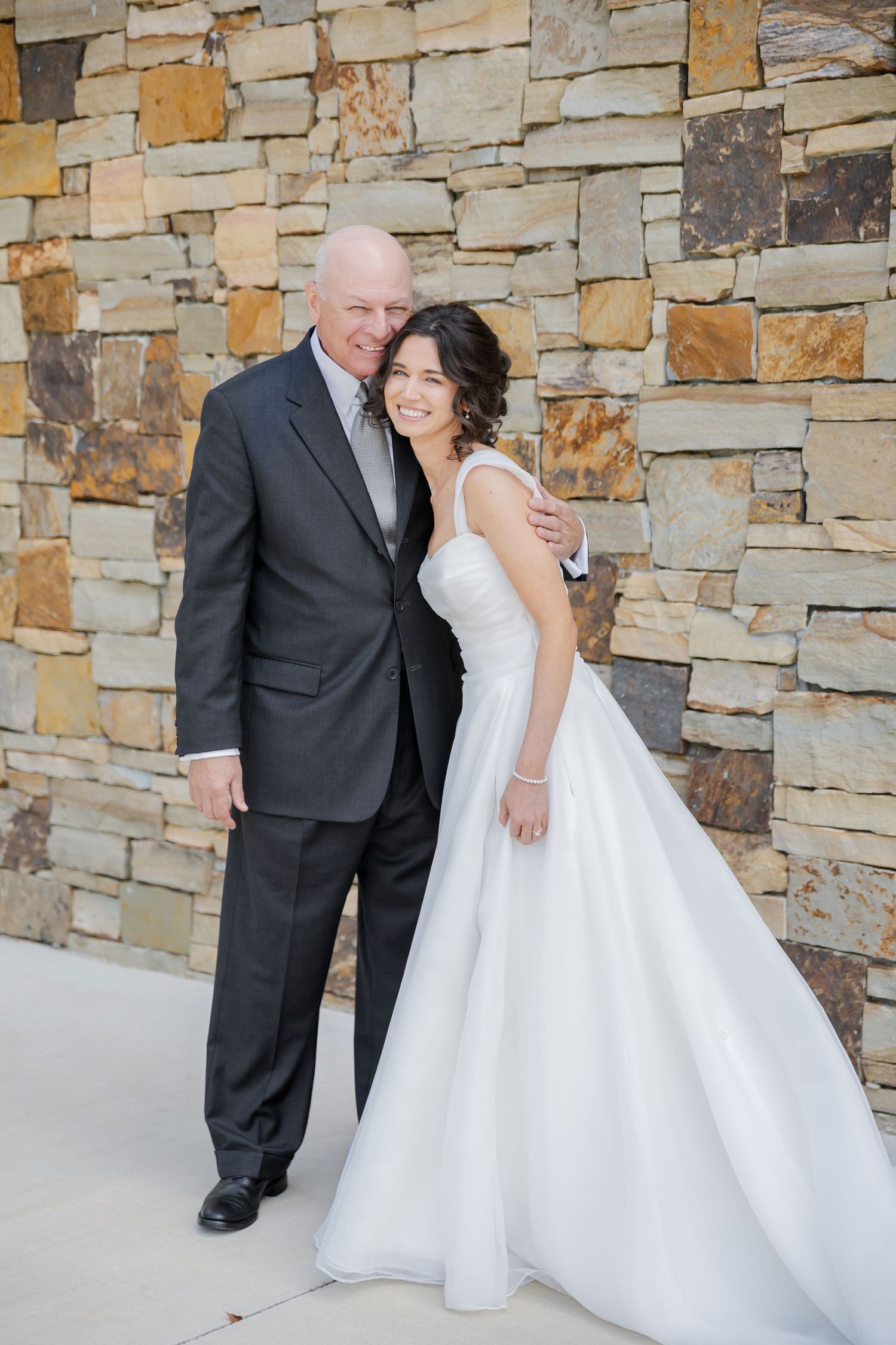 Newlywed couple shares intimate moments against rustic stone wall backdrop during wedding photoshoot.
