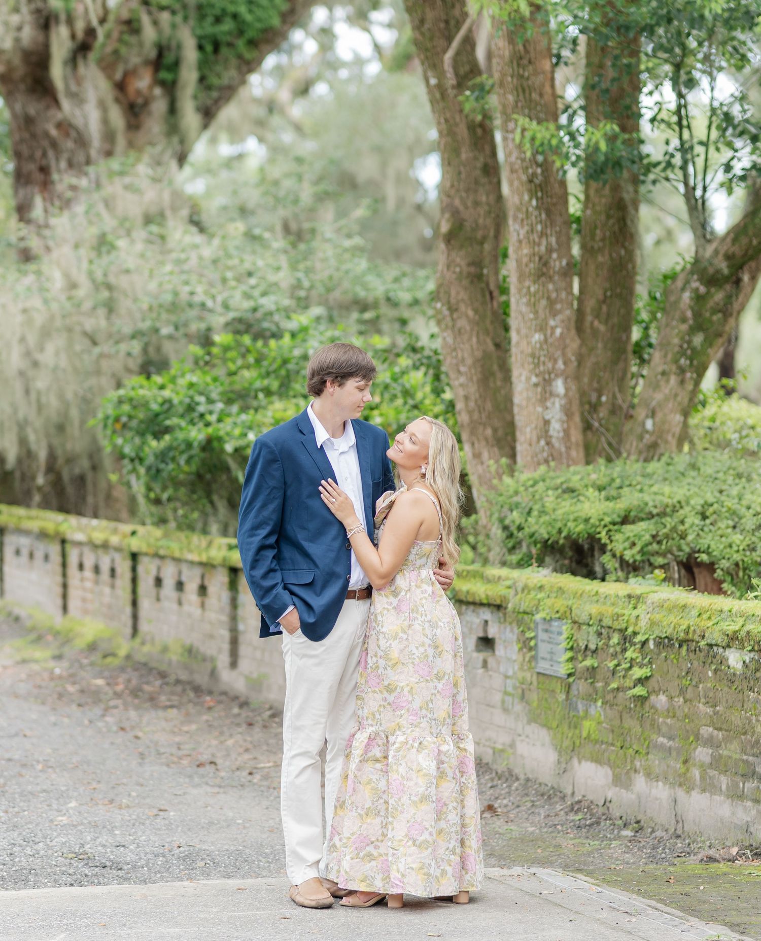 Romantic engagement photos captured along a tree-lined path with Spanish moss hanging overhead.