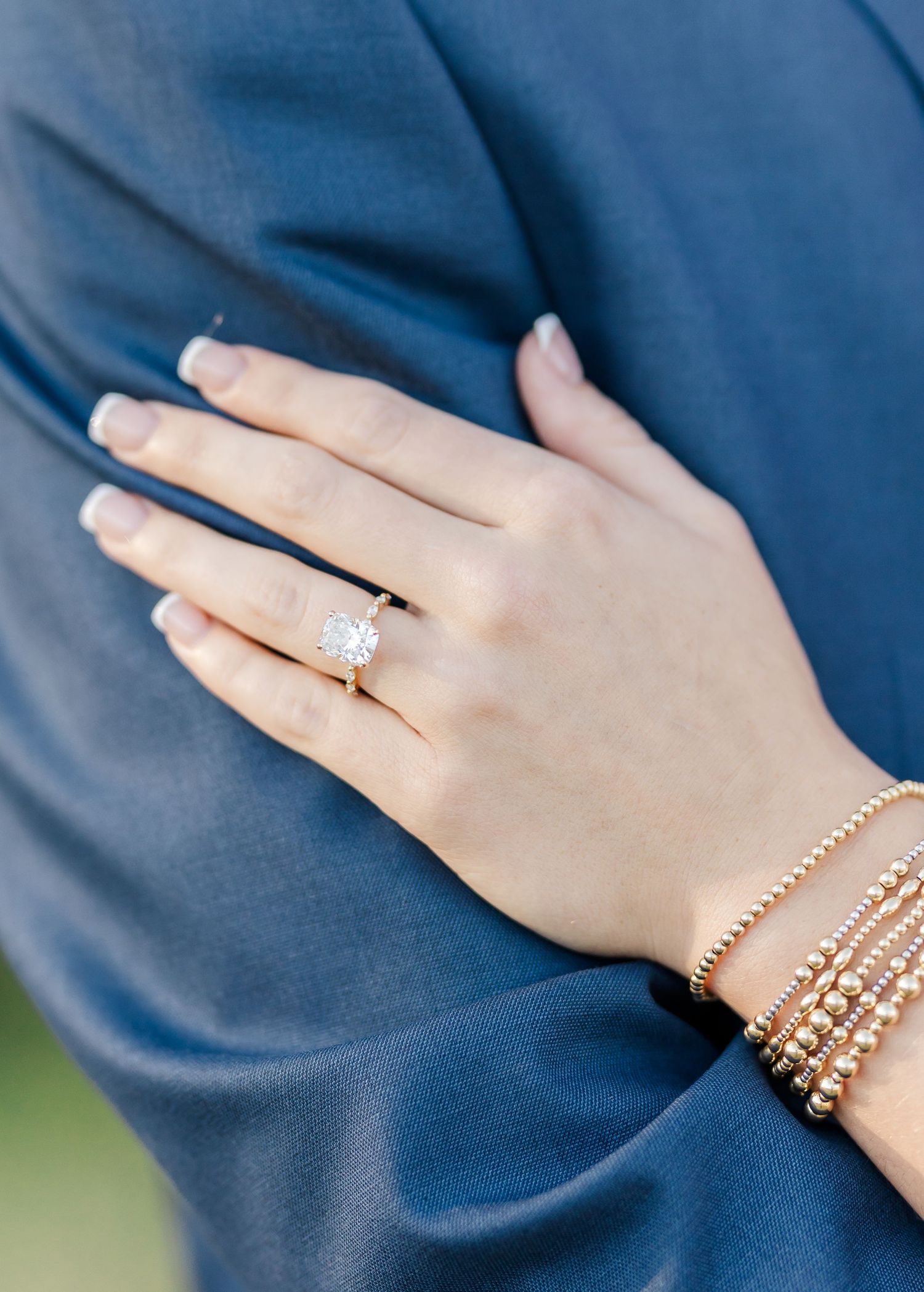 Close-up view of an engagement ring and rose gold bracelets on a hand against a blue background.