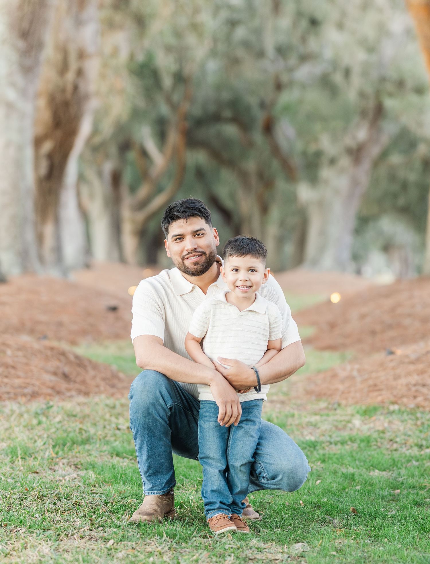 Father and young child share a joyful moment together outdoors under a canopy of trees.