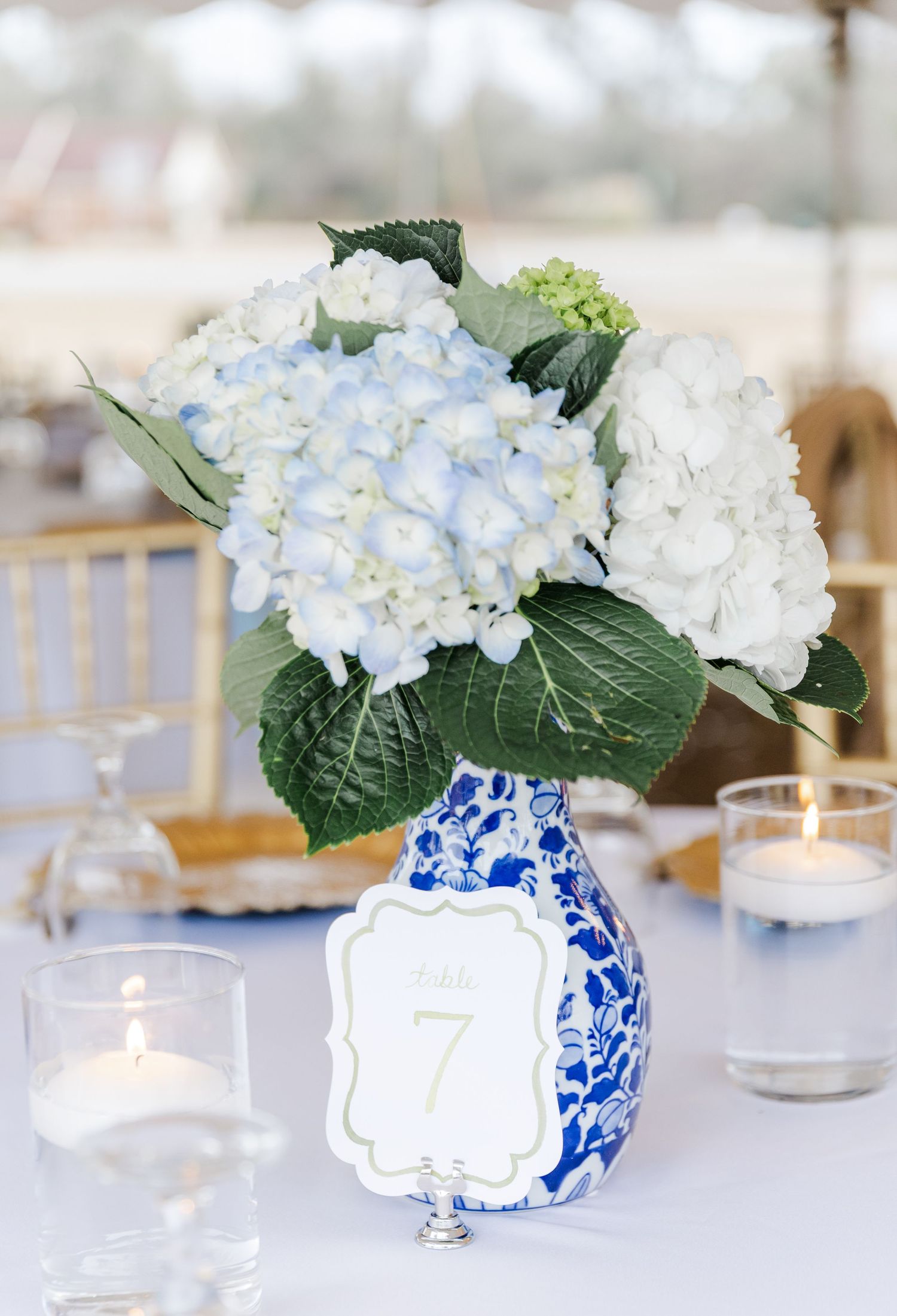 Blue and white chinoiserie vase with white hydrangea centerpiece and table number 7 at elegant wedding reception.