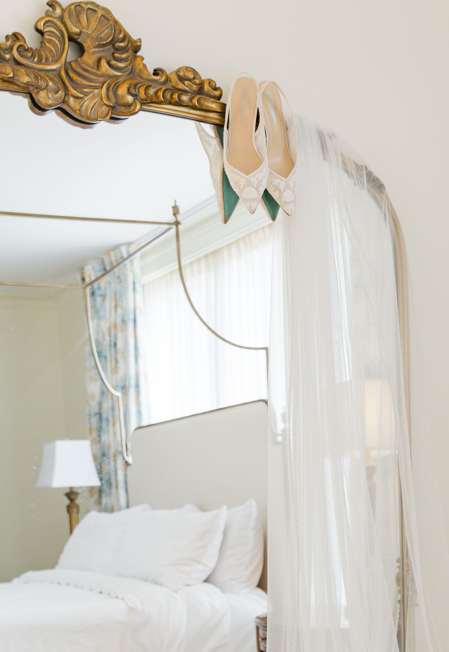 Bridal heels and veil draped over ornate gold mirror in elegant bedroom.