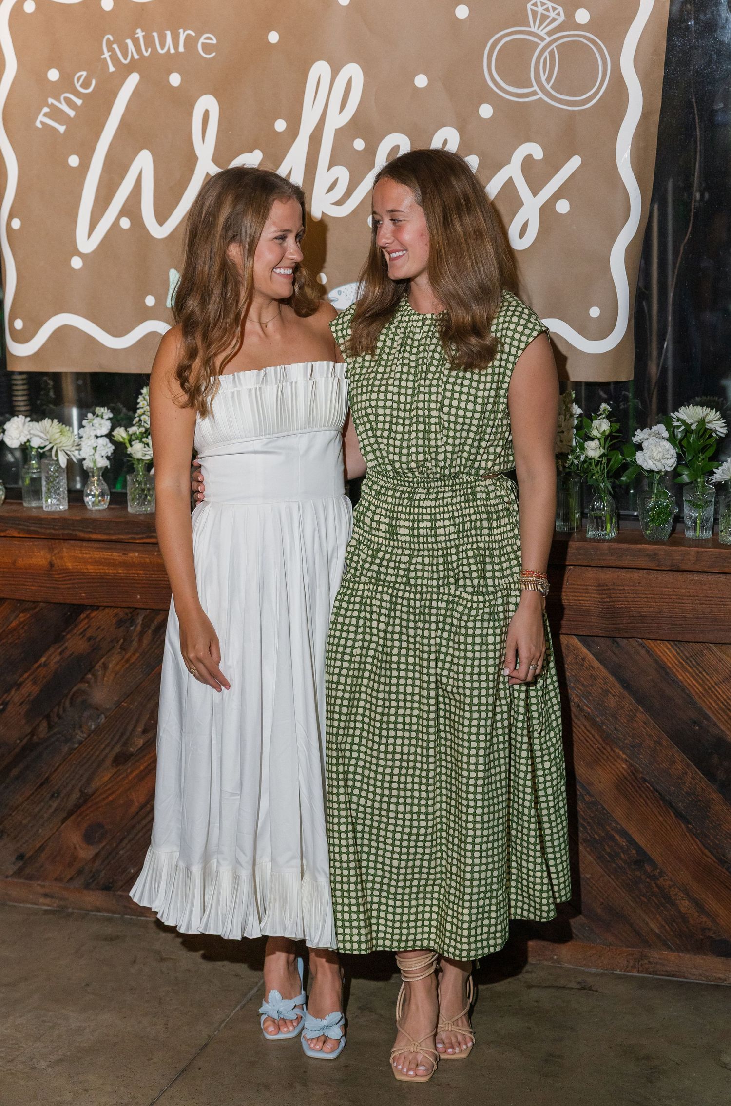 Two women in elegant green and white midi dresses pose at 'The Future Walkers' engagement party.