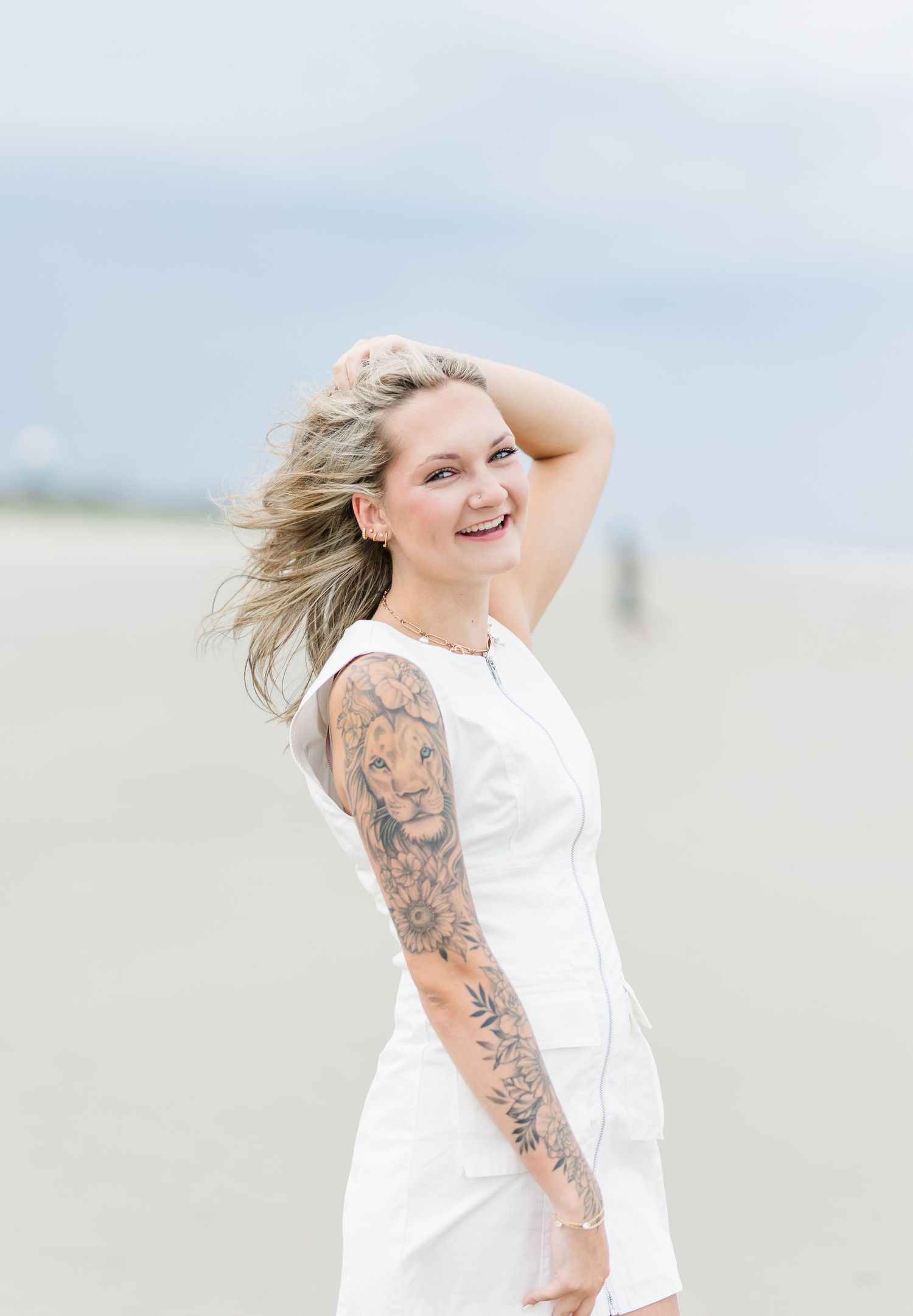 Joyful beach photo with white sundress and lion tattoo sleeve in soft natural lighting.