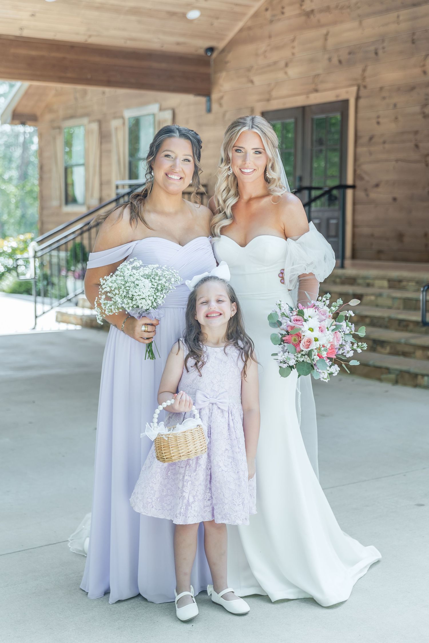 Bridal party members pose together on concrete porch of rustic wooden venue.