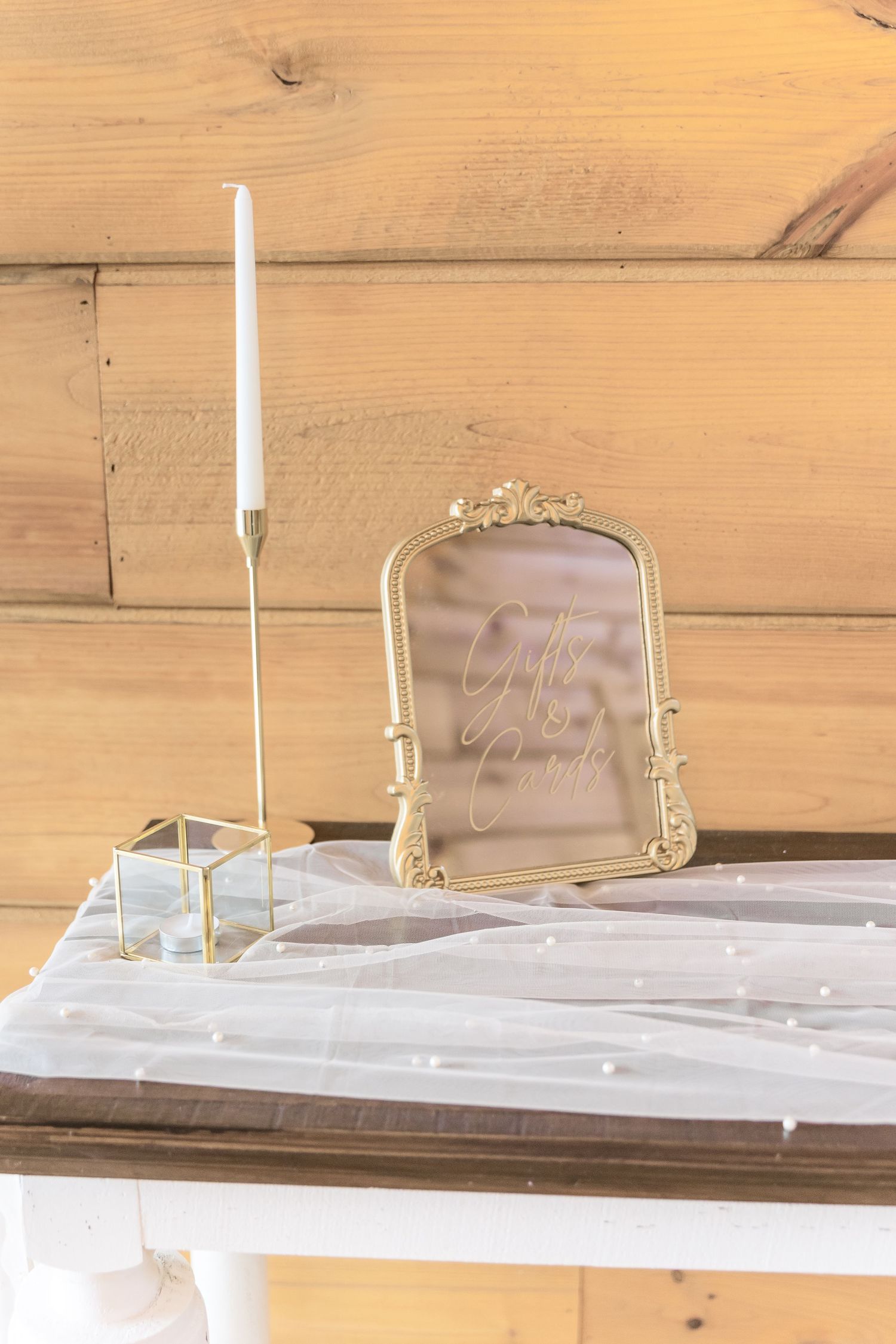 Elegant gold-framed sign and white taper candle holder on draped table.